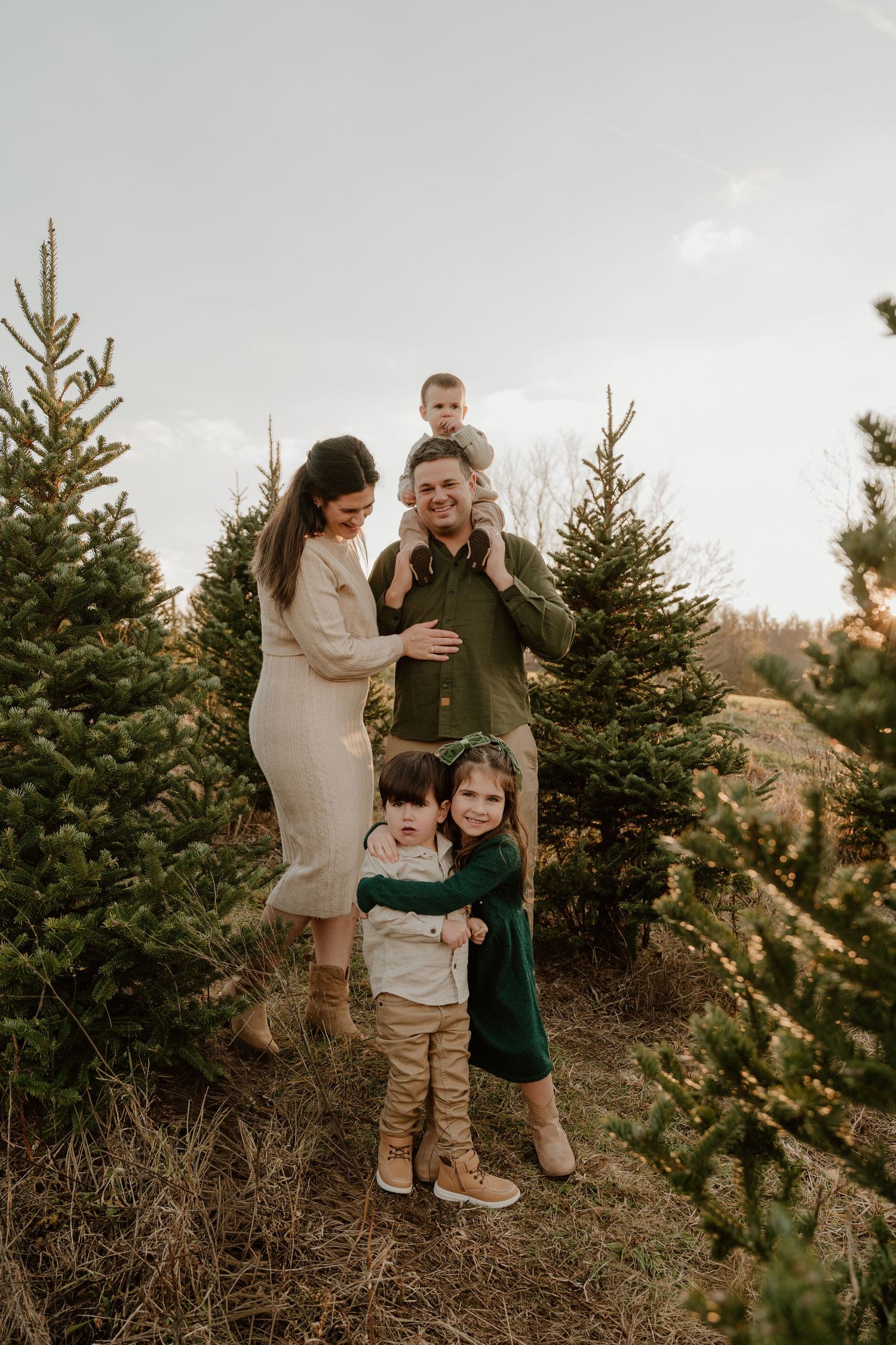 A family shares tender moments together among evergreen trees during a golden hour outdoor photo session.