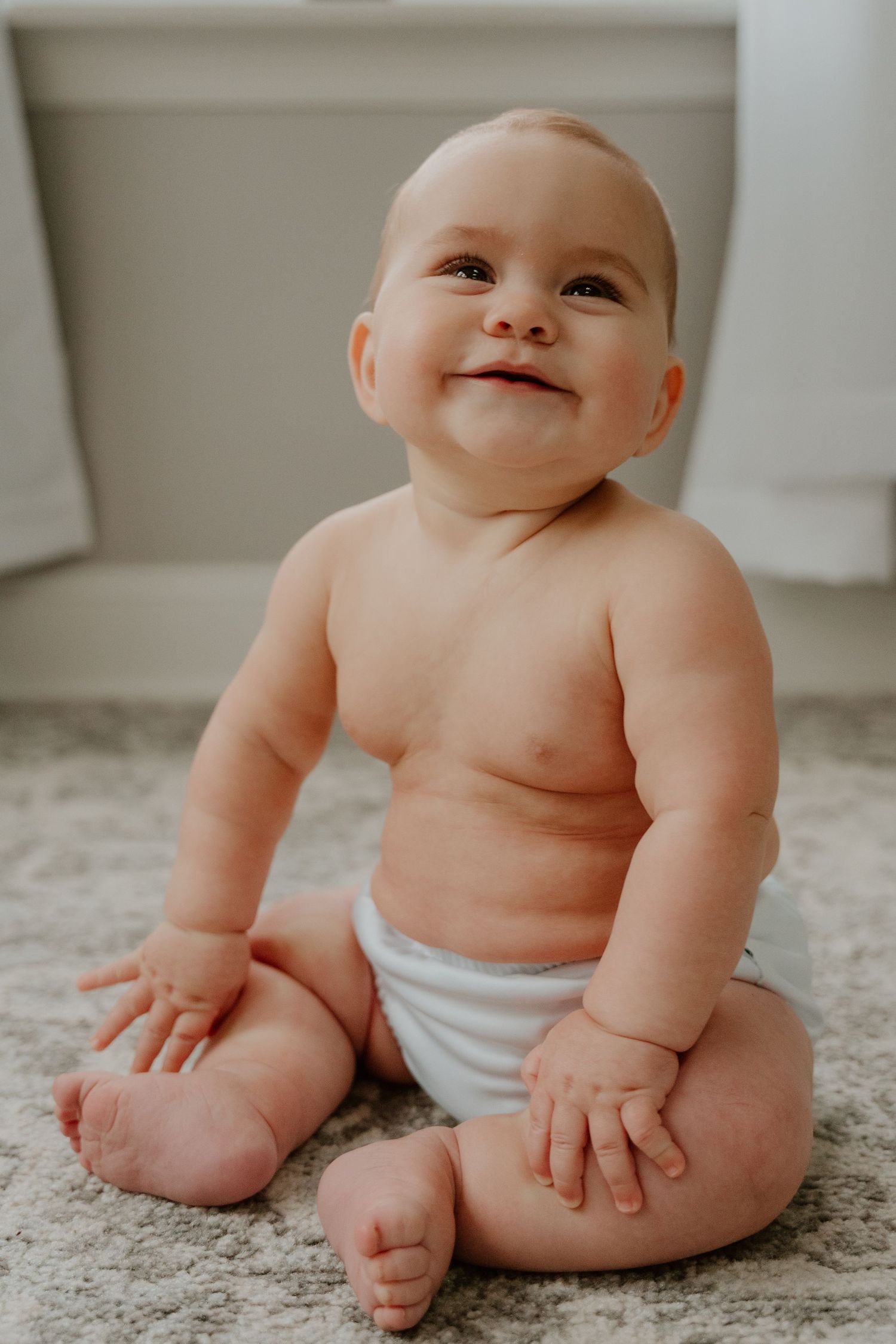 A series of sweet photos showing a baby in a diaper sitting and playing on a light colored carpet.