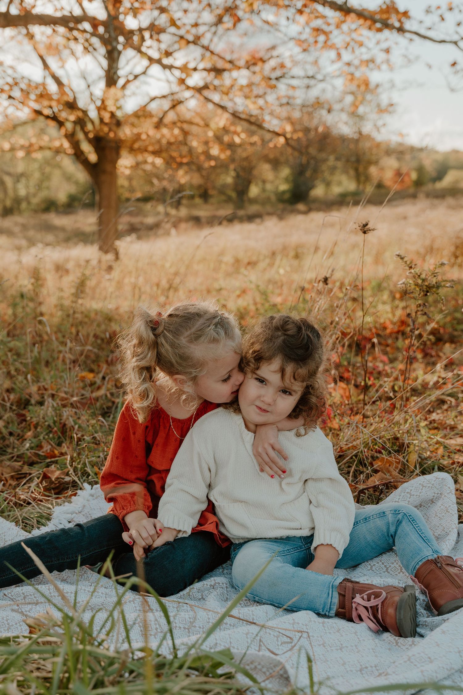 Children laying on a blanket outdoors in autumn with golden leaves and red berries in the background.