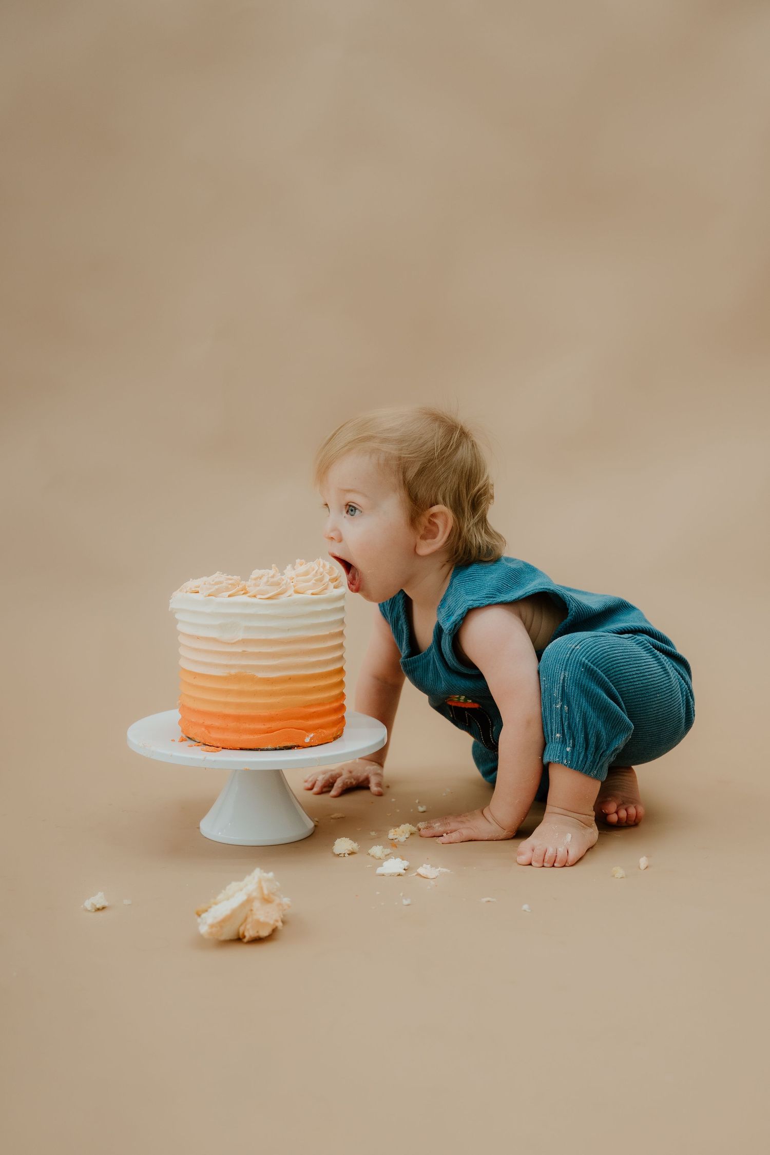 A progression of four photos showing a small child in teal crawling towards and tasting an orange ombre cake.