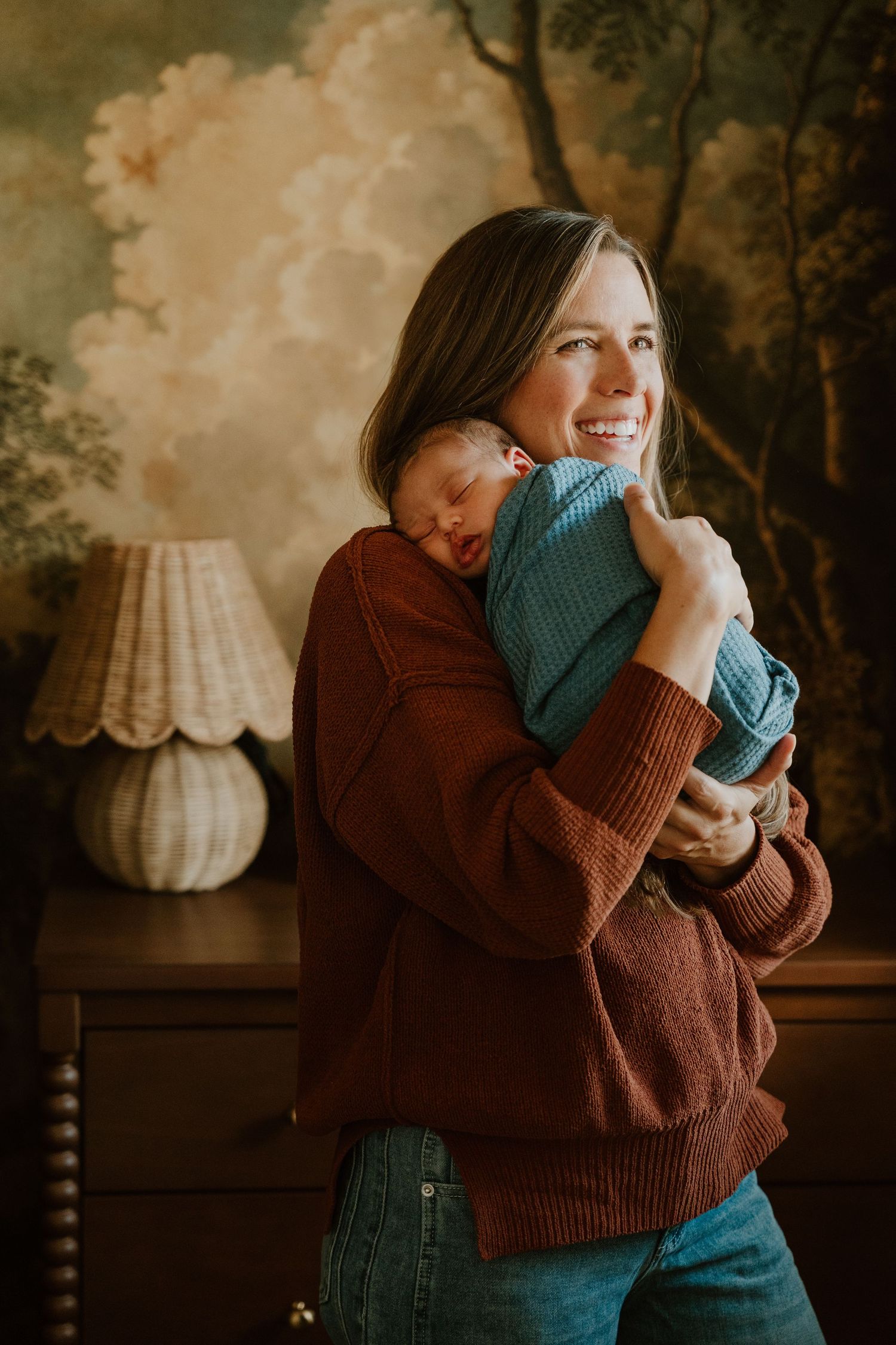 A warm indoor portrait showing tender moments between parent and baby in cozy autumn sweaters by a vintage lamp.