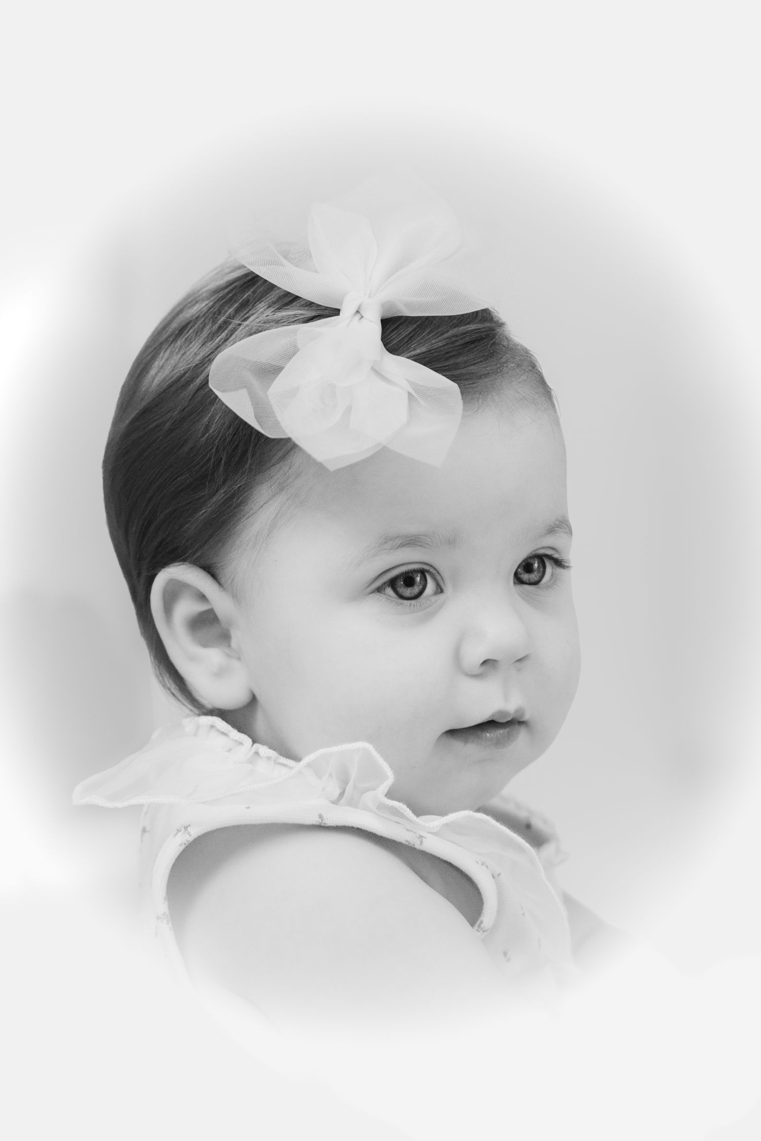 A soft black and white artistic photo collage showing three gentle side profile views of a baby wearing a white bow.