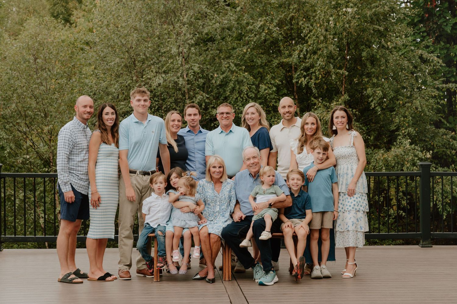 A large extended family group poses together outdoors in coordinated blue and white outfits for a photo session.