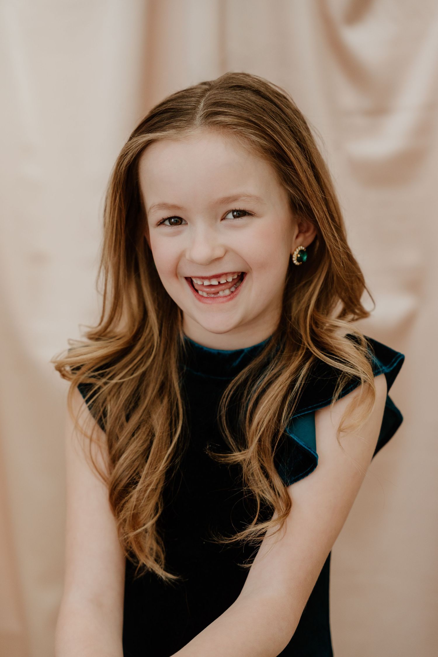 Portrait of someone wearing a black sleeveless top against a beige background with a bright joyful expression.