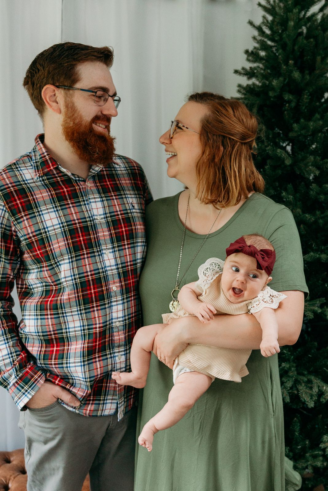 A family poses together near a Christmas tree in casual winter attire.