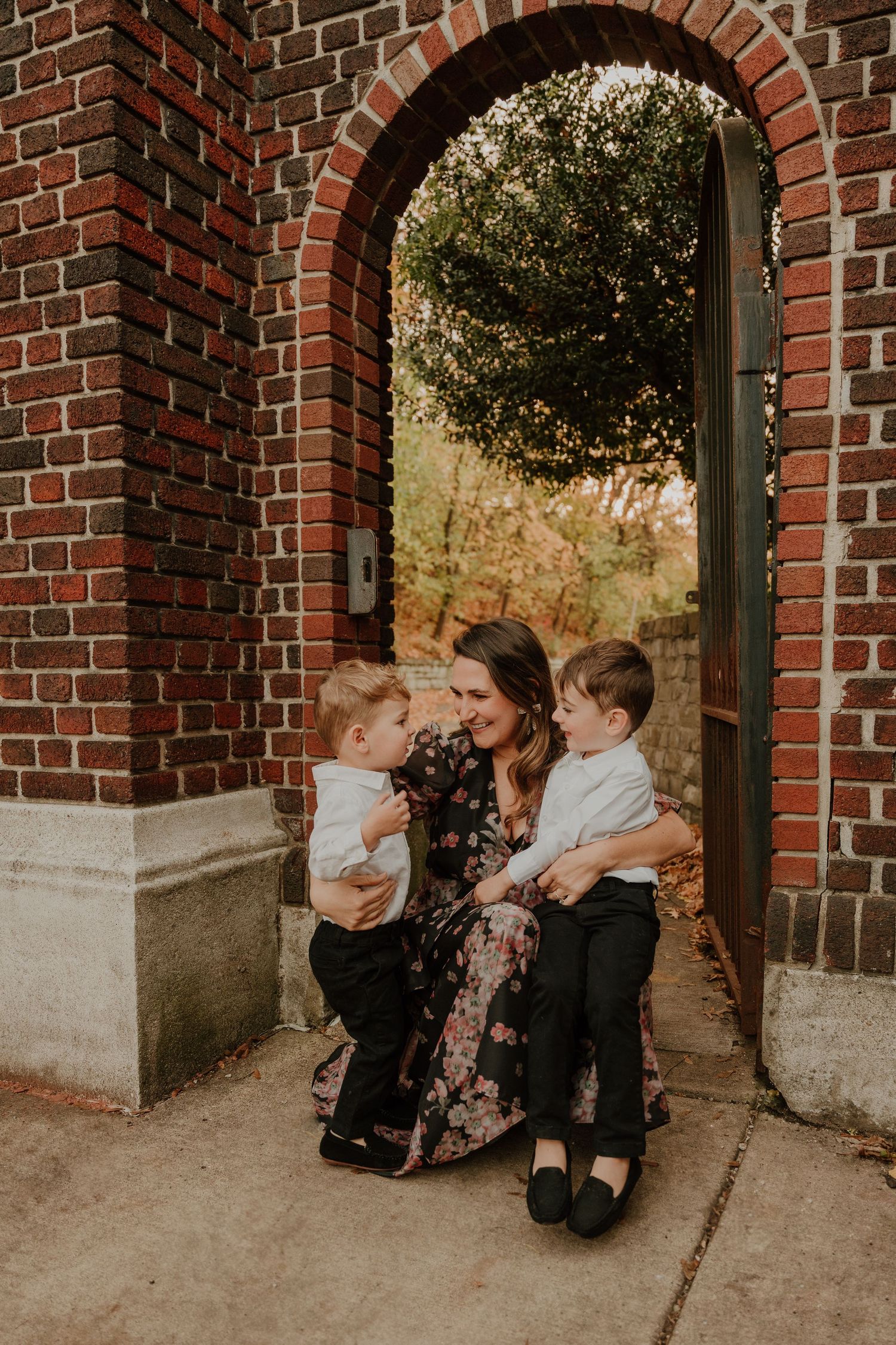 Family sharing tender moment together under brick archway in warm sunlight.