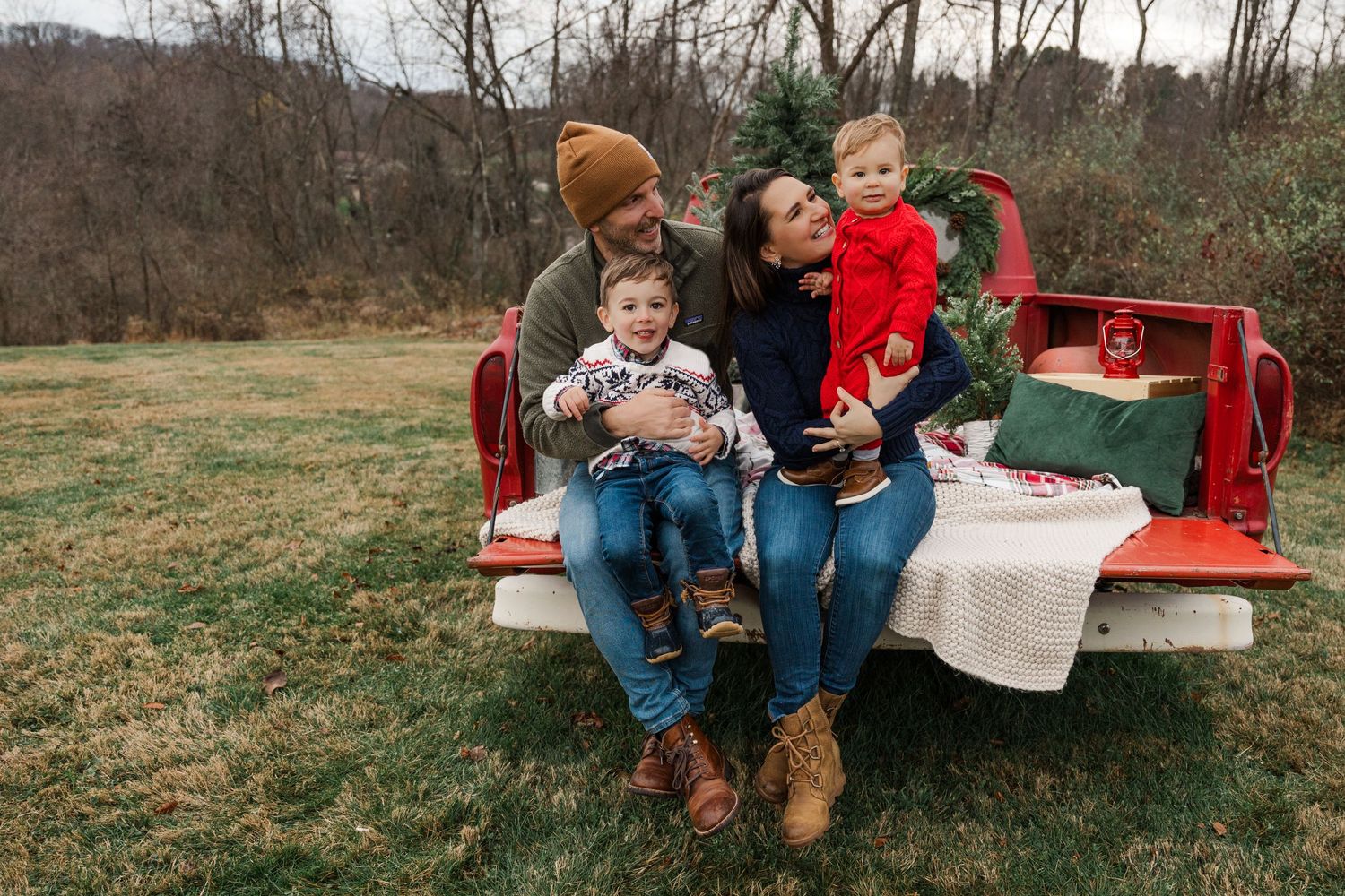 Family sitting together on red vintage truck tailgate in rural setting.