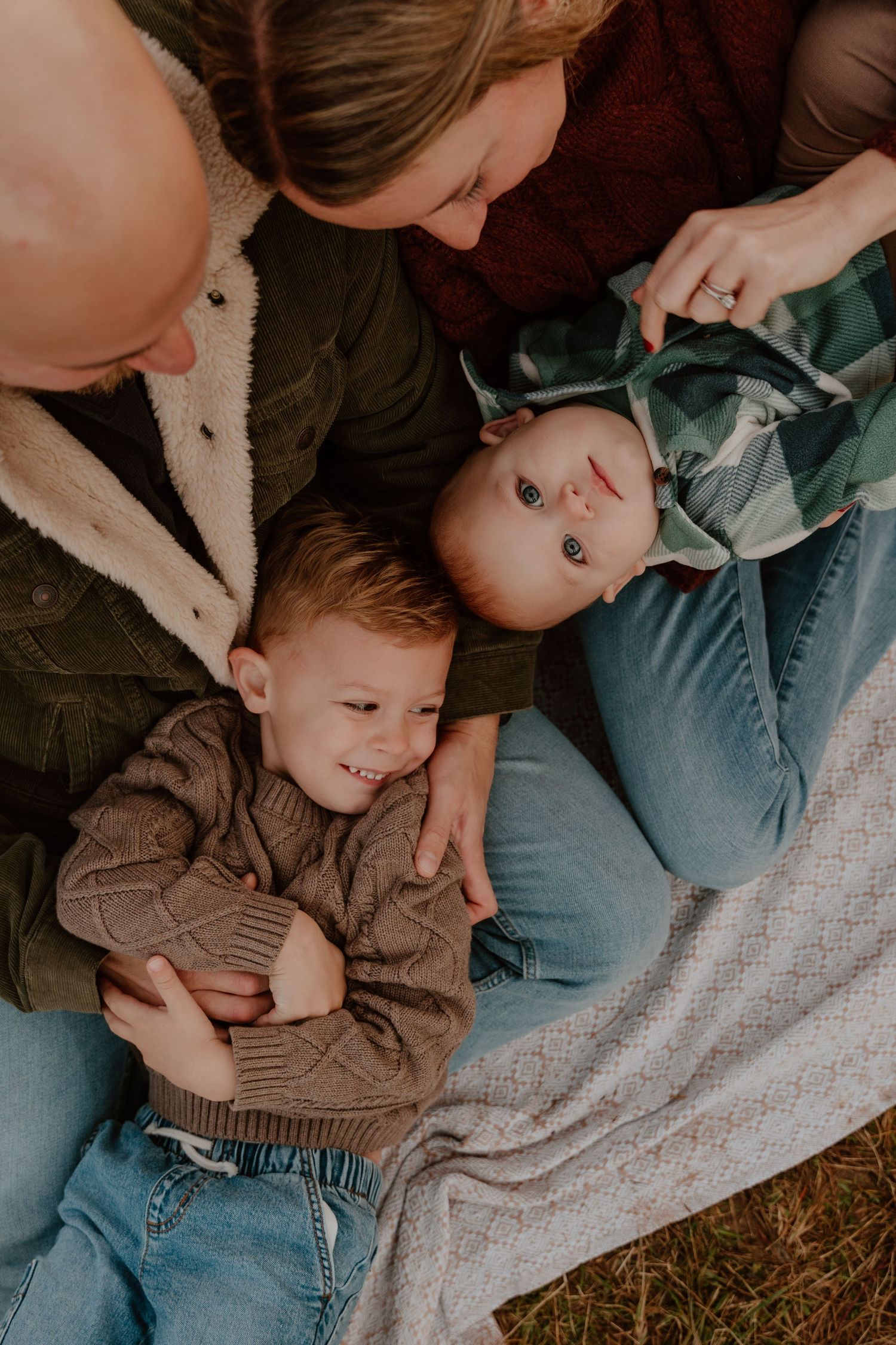Overhead view of a family lying together on a blanket outdoors, sharing an intimate bonding moment.