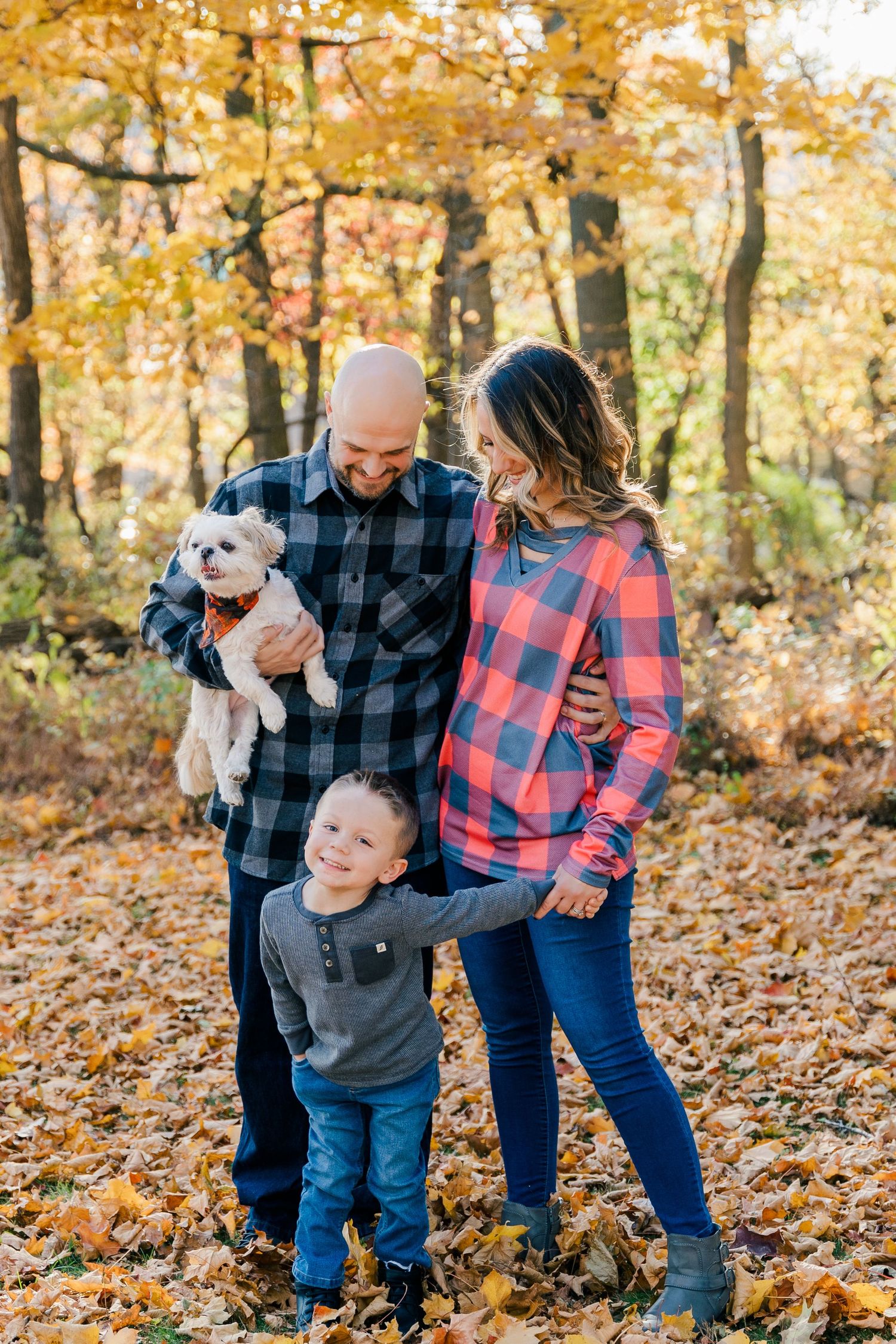 Family in plaid shirts posing together in golden autumn forest with stuffed animal.