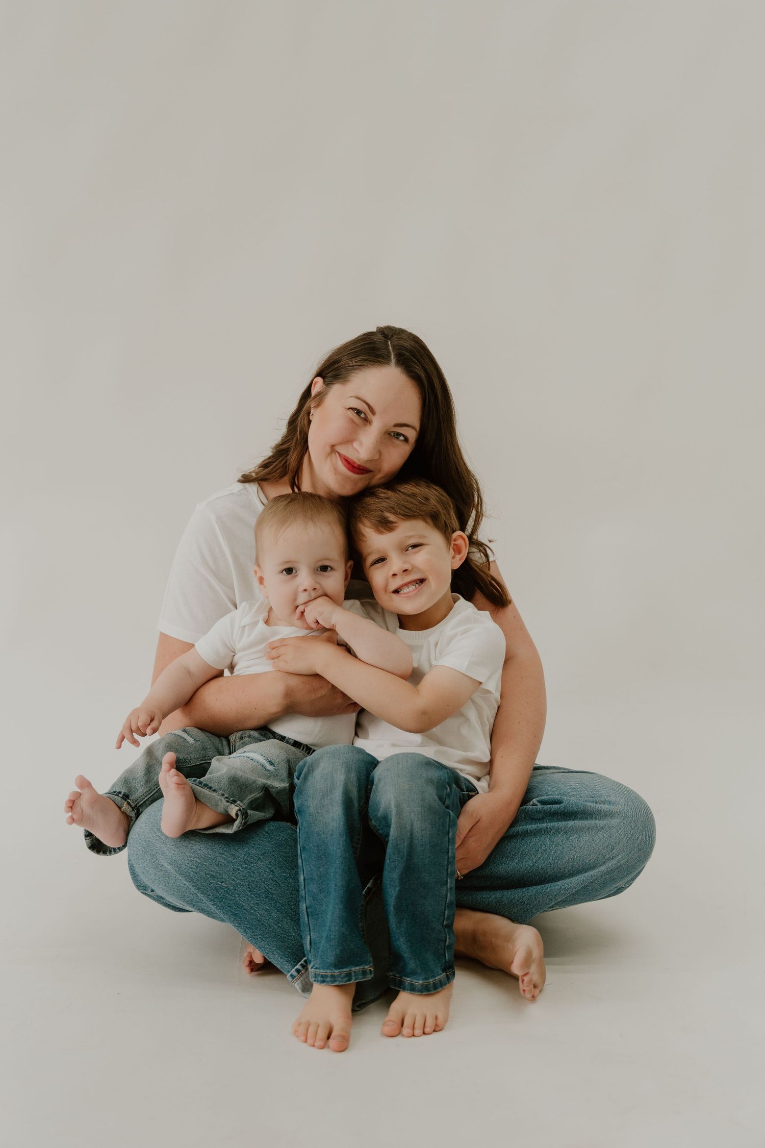 A family sits together on the floor wearing casual white shirts and jeans against a neutral background.
