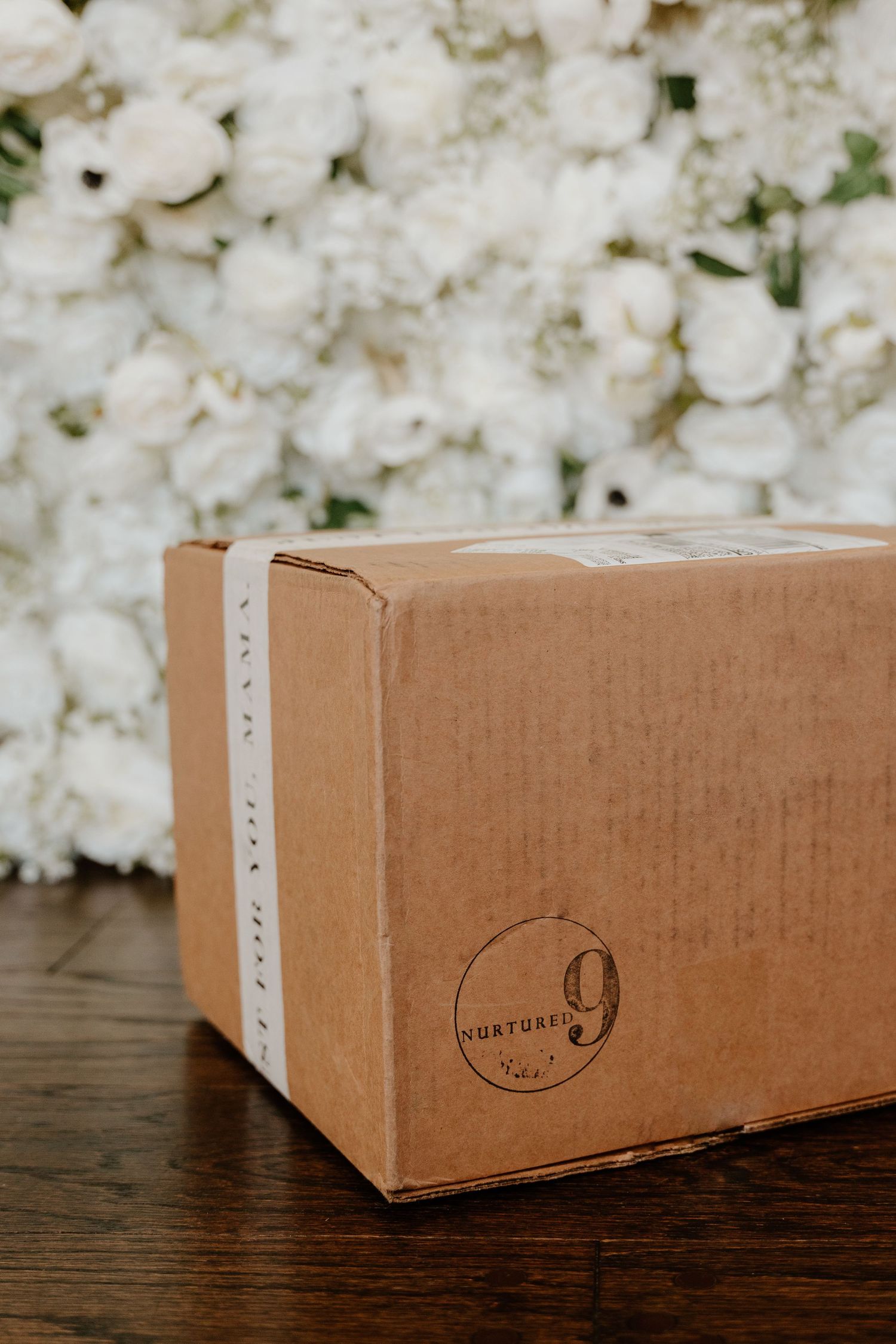 Brown cardboard boxes with logo displayed against white floral background and dark wooden surface.