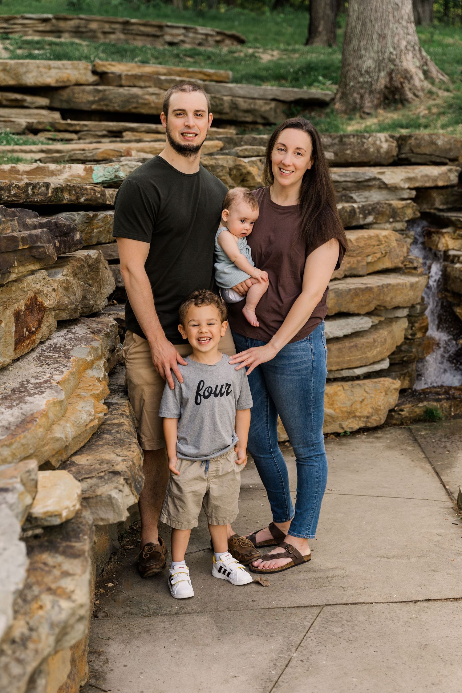 Family portrait on stone steps near waterfall in natural setting.