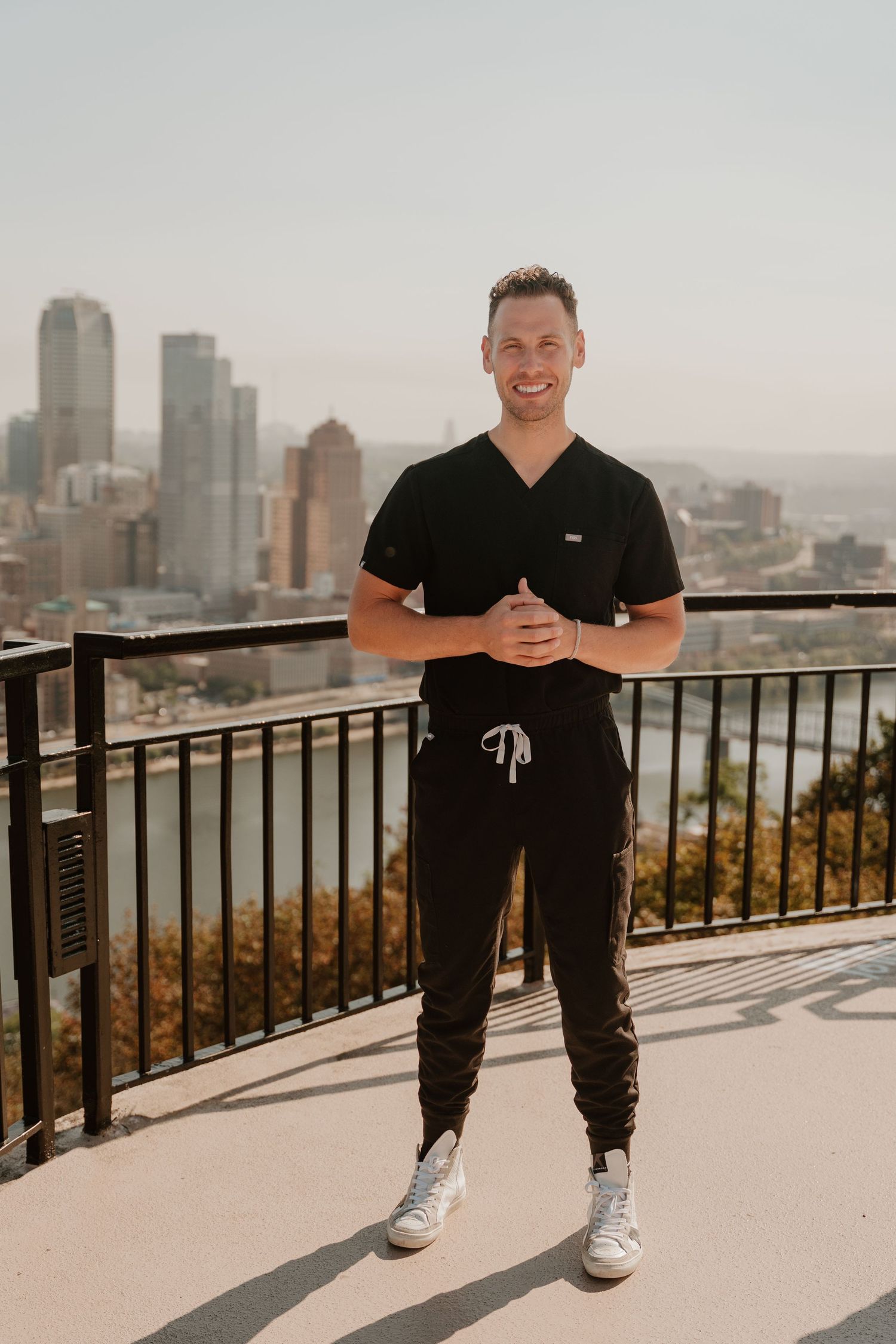 Person in black clothing poses against city skyline backdrop on sunny observation deck.