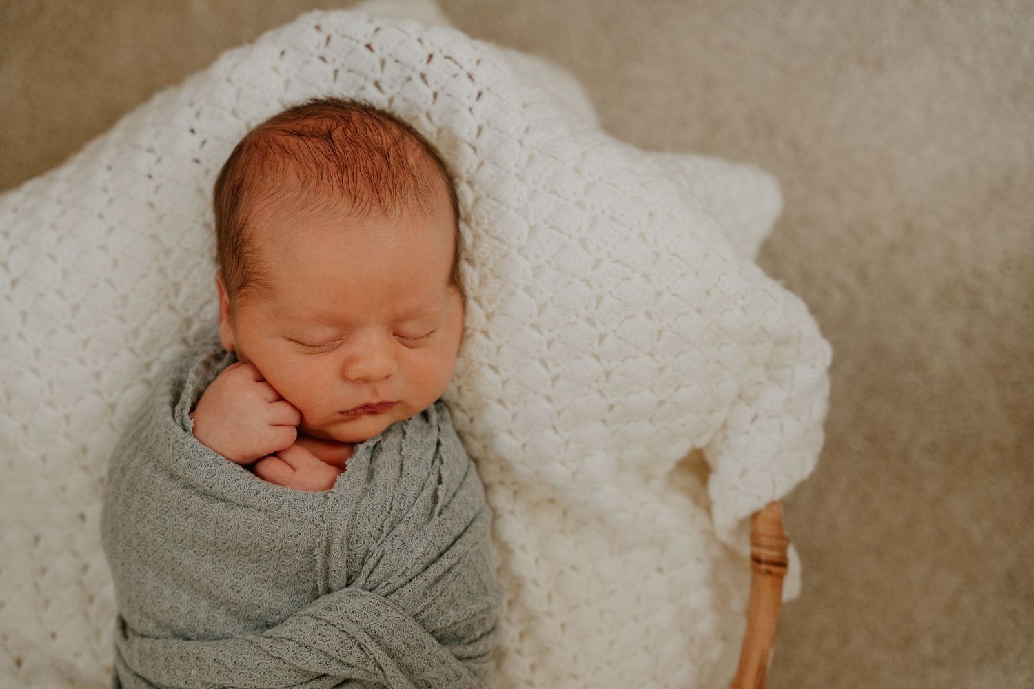 A sleeping newborn baby swaddled in gray fabric lies peacefully on a soft white blanket.