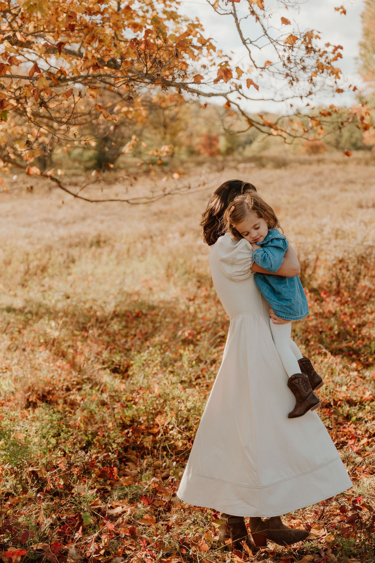 A child in a white dress twirls playfully among autumn leaves during a fall photo session in warm golden light.
