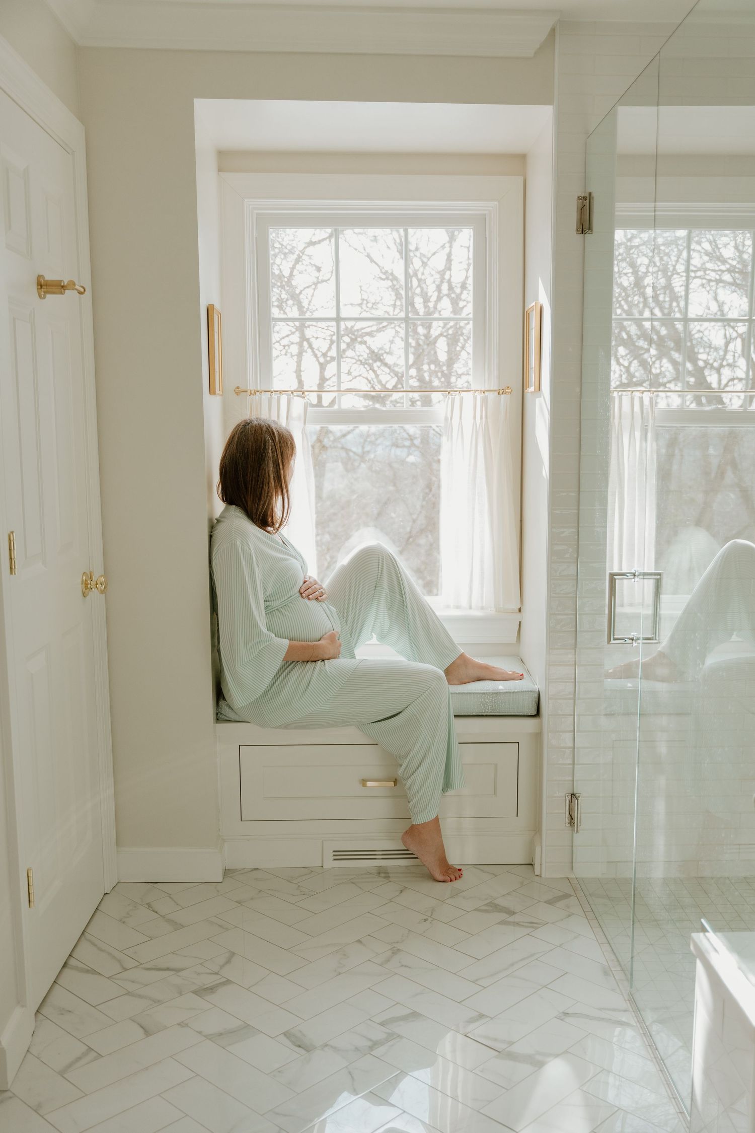 Multiple frames show a person in mint green clothing sitting on a white windowsill in a bright modern bathroom.