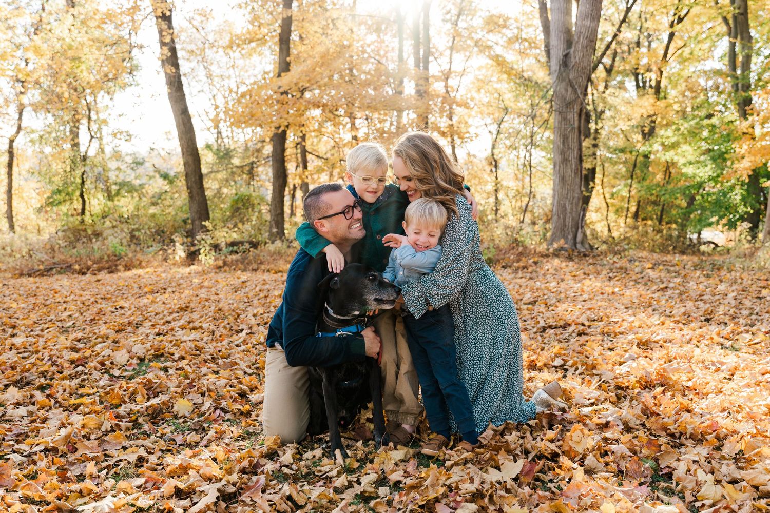 Family sitting together on fallen autumn leaves in wooded setting.