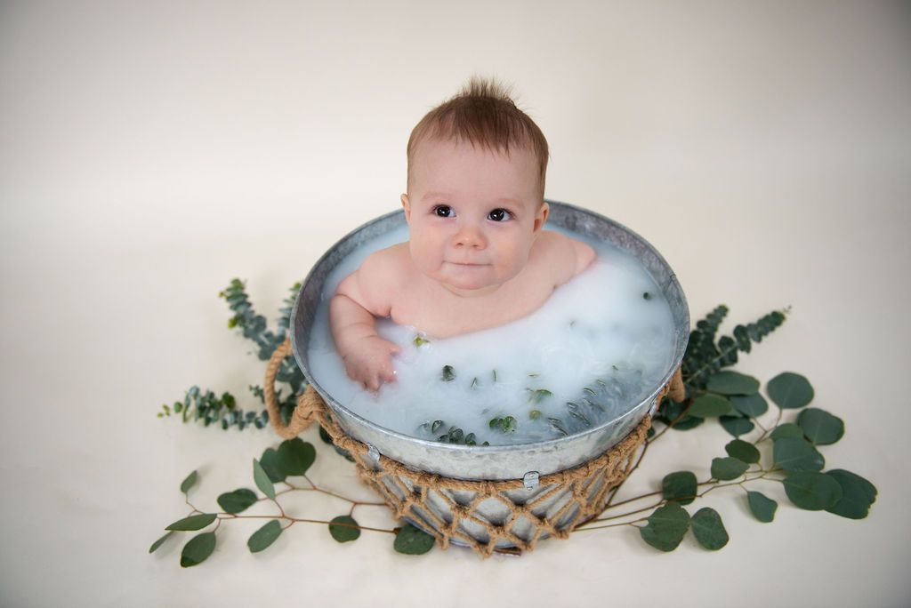 Baby in dreamy milk bath photo with greenery and woven basket.