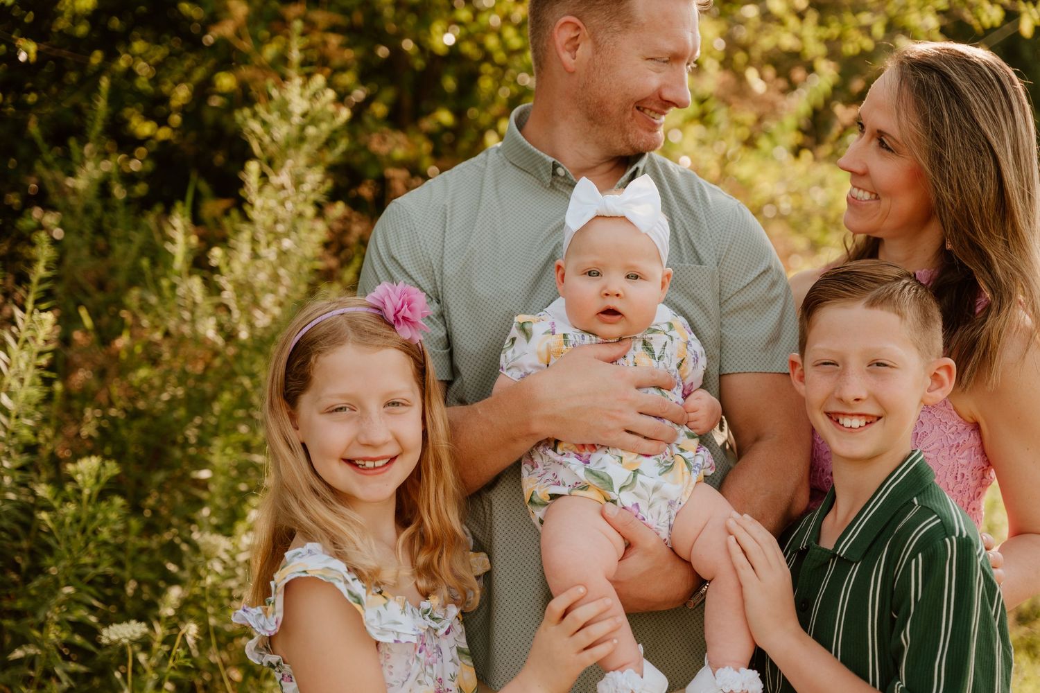 A joyful family laughs together outdoors during a sunny portrait session in nature.