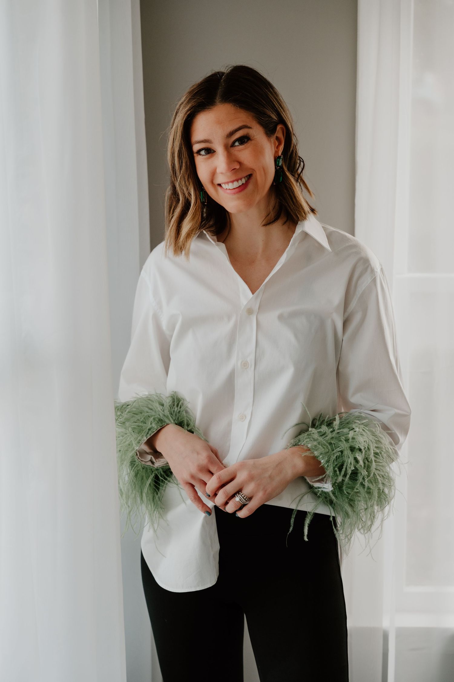 Woman in white button-down shirt with green feather trim cuffs poses against light background in fashion photo series.