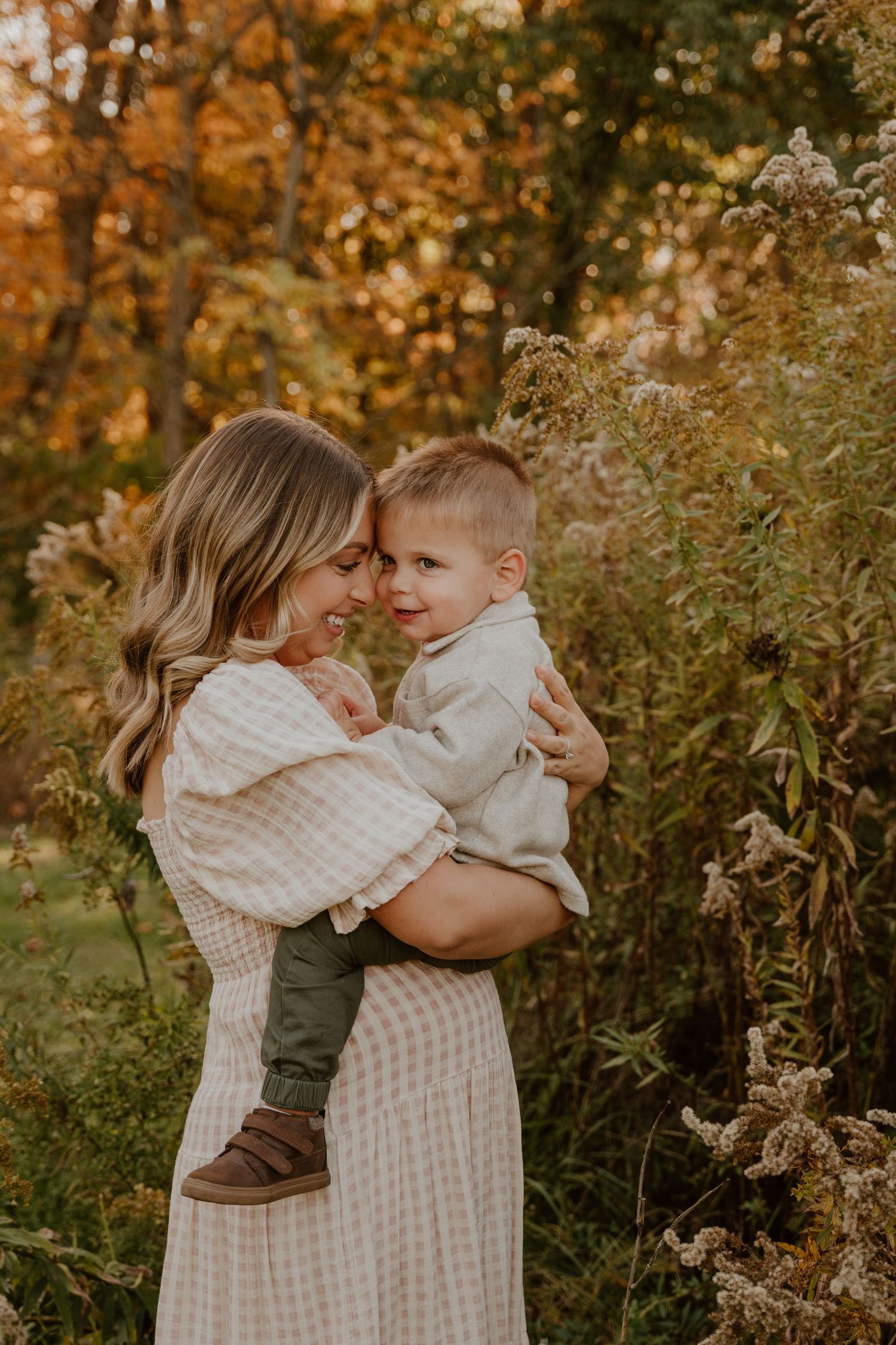 A tender autumn scene with a parent and child embracing outdoors among golden foliage and tall grasses.