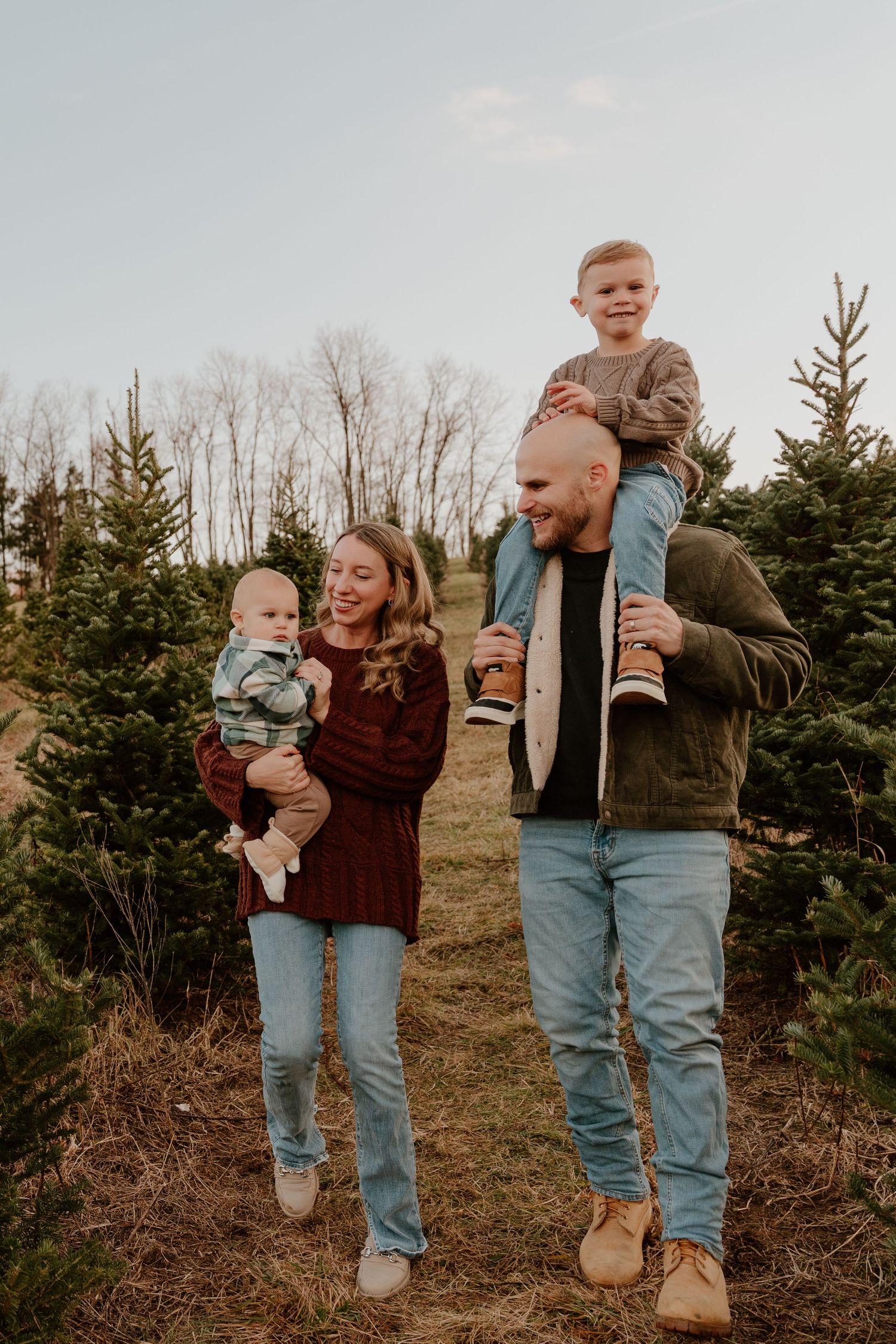 A group poses together outdoors among evergreen trees on a winter day wearing casual sweaters and jeans.