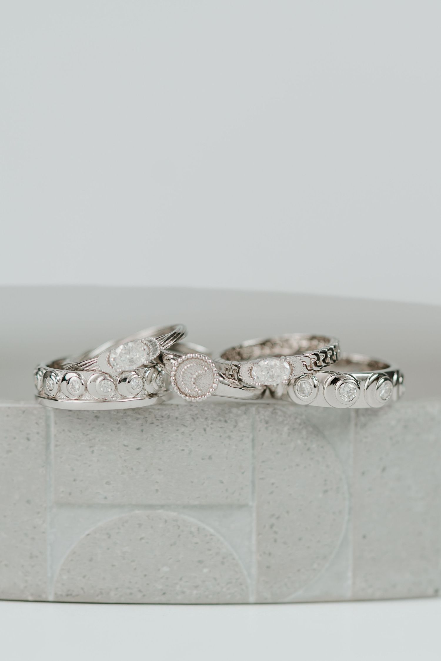 Delicate vintage-style silver rings with intricate scroll designs arranged on a white stone surface.