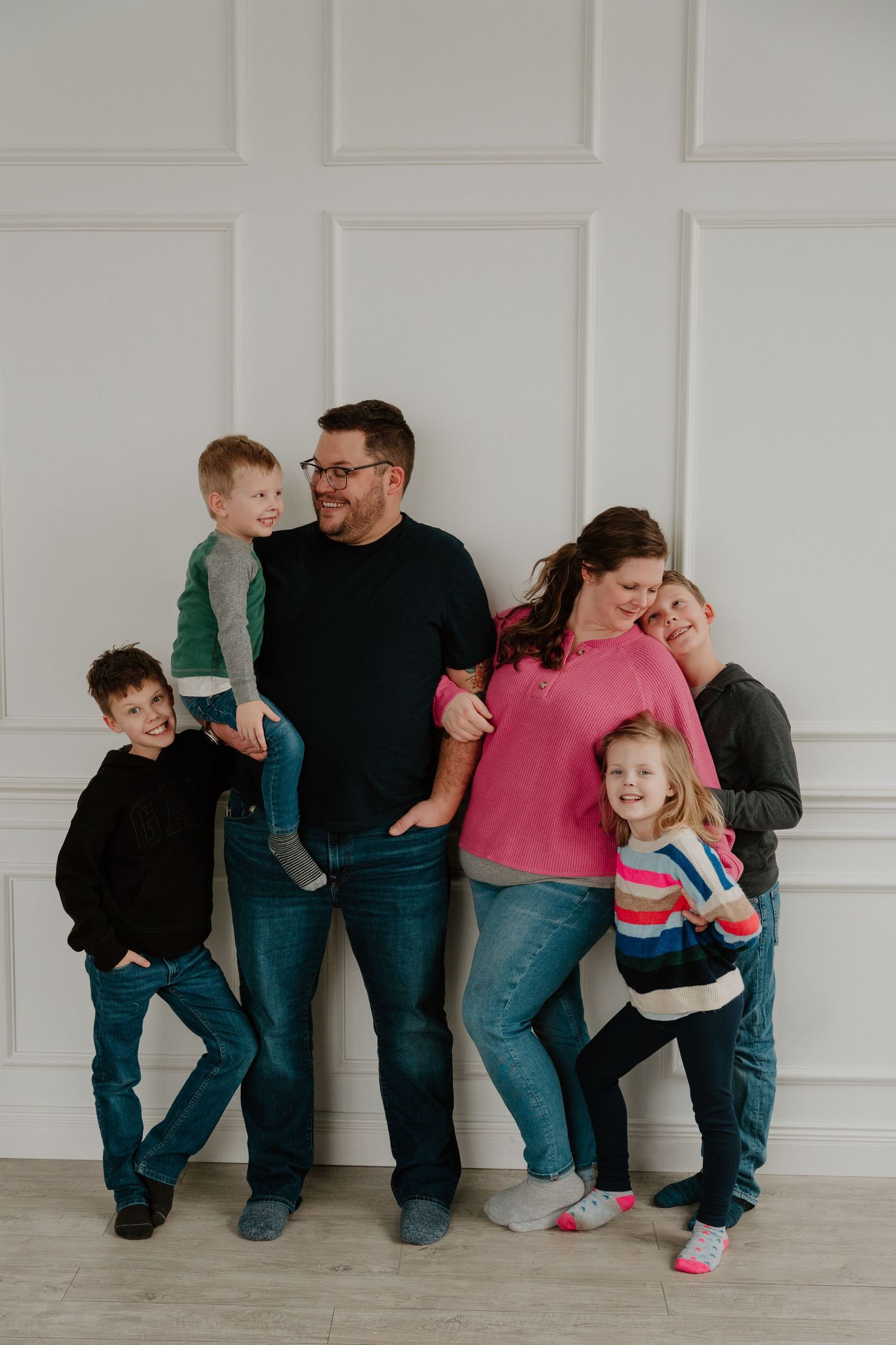 A playful family photo series showing casual poses against a white wall while wearing jeans and casual attire.
