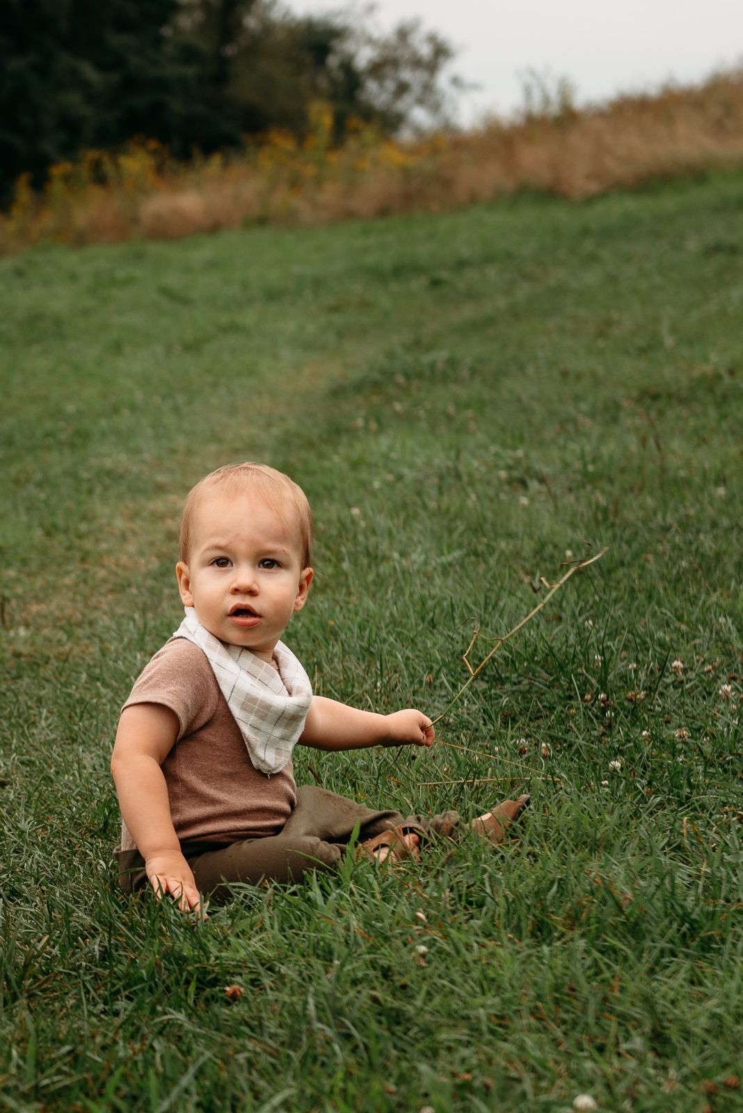 Small child sitting in grass on hillside during summer day.