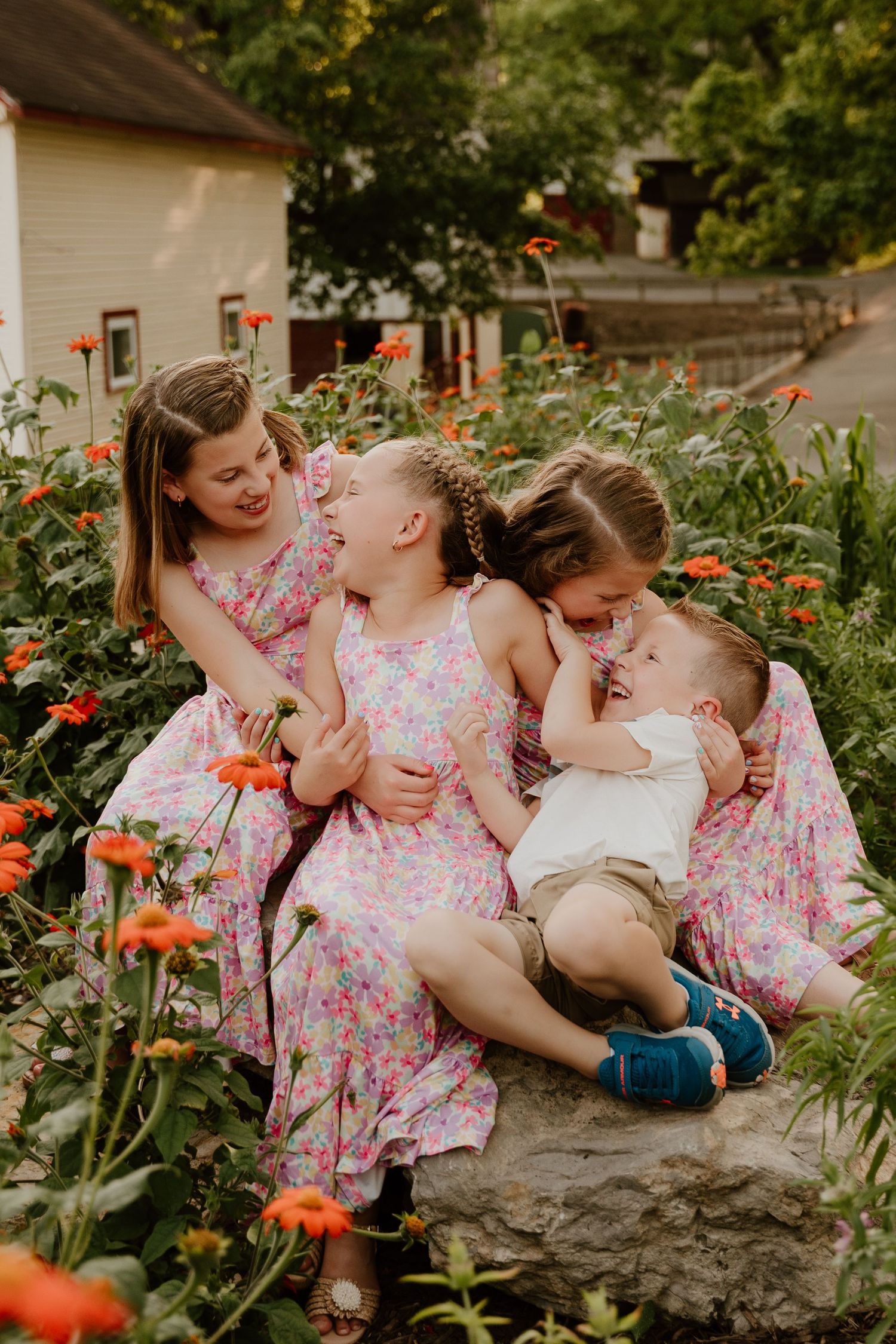 Three figures in matching floral dresses share a joyful moment together among orange flowers in a garden setting.