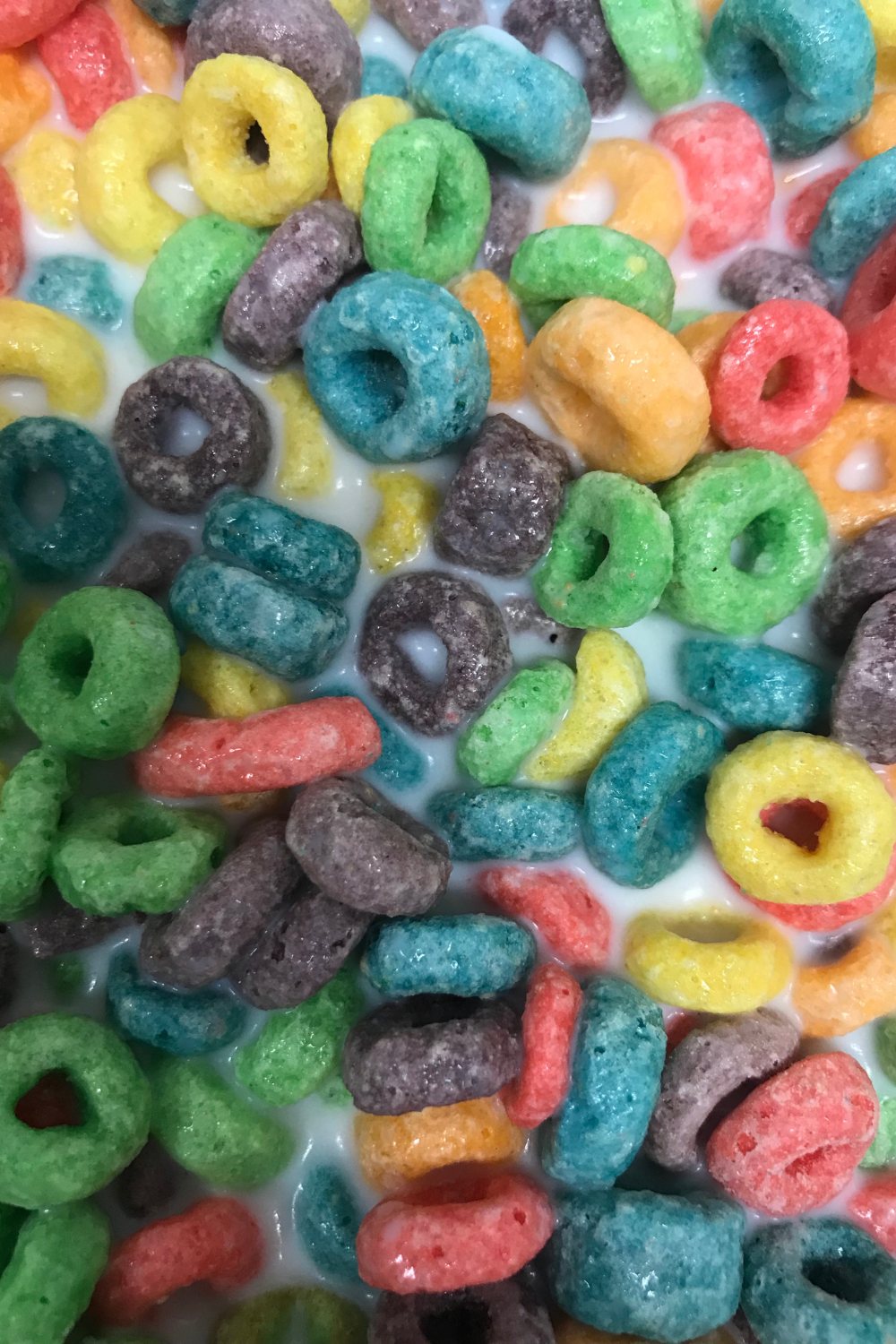 Colorful fruit loops cereal scattered in milk creating bright rainbow pattern.