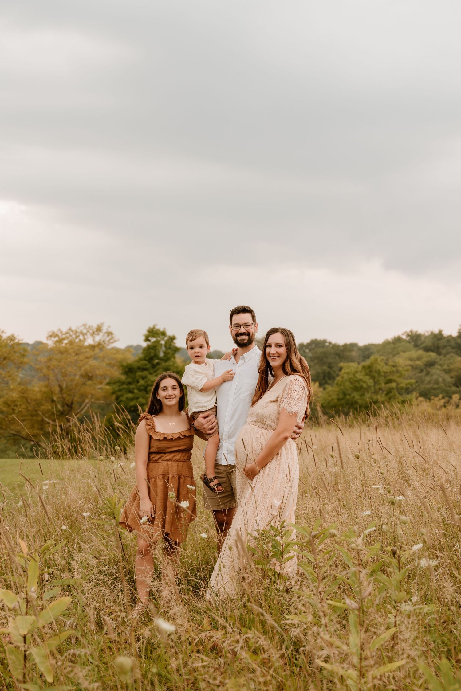 Family standing together in golden field during sunset photoshoot.