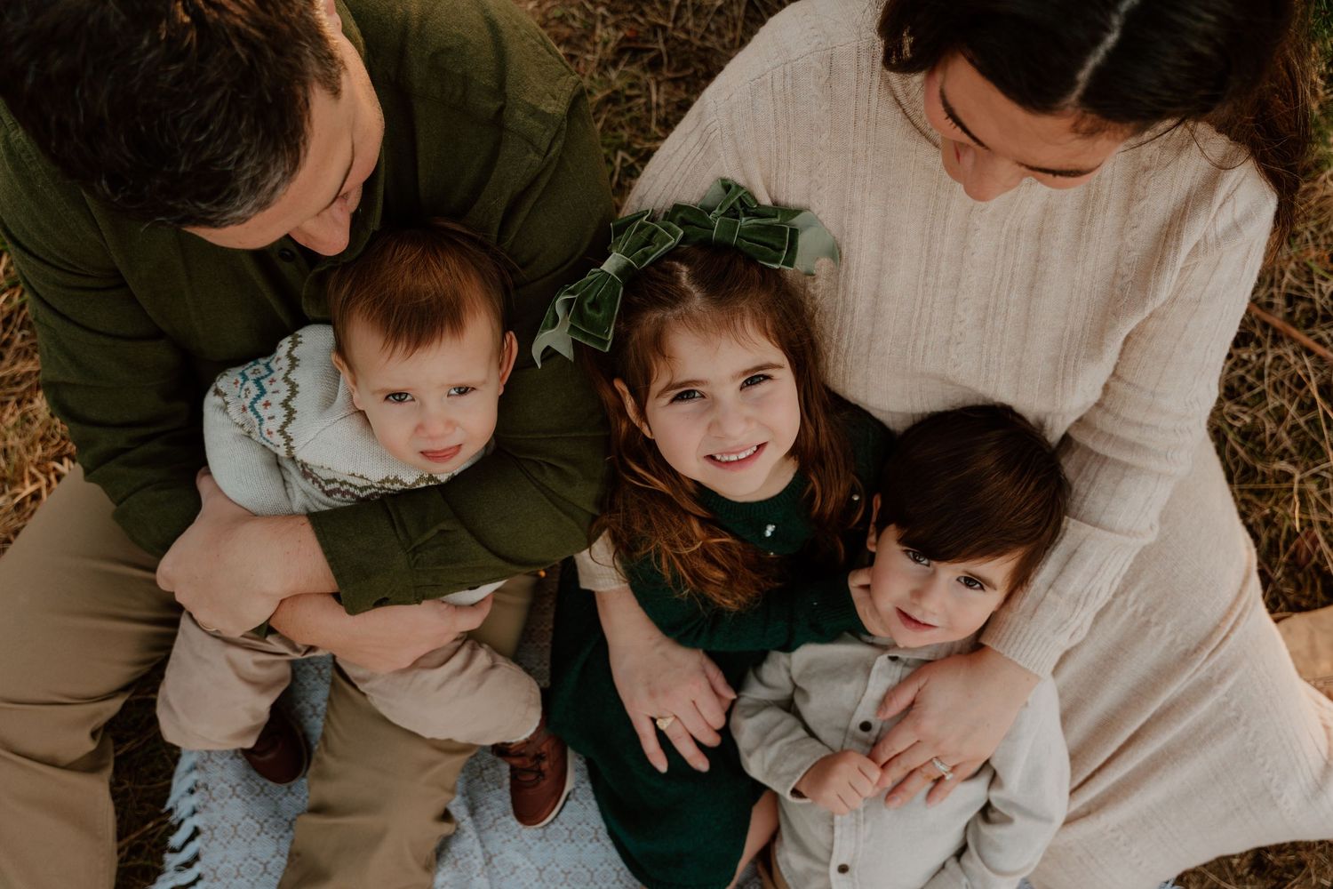 A family cuddles together on a blanket while sharing tender moments and embraces.
