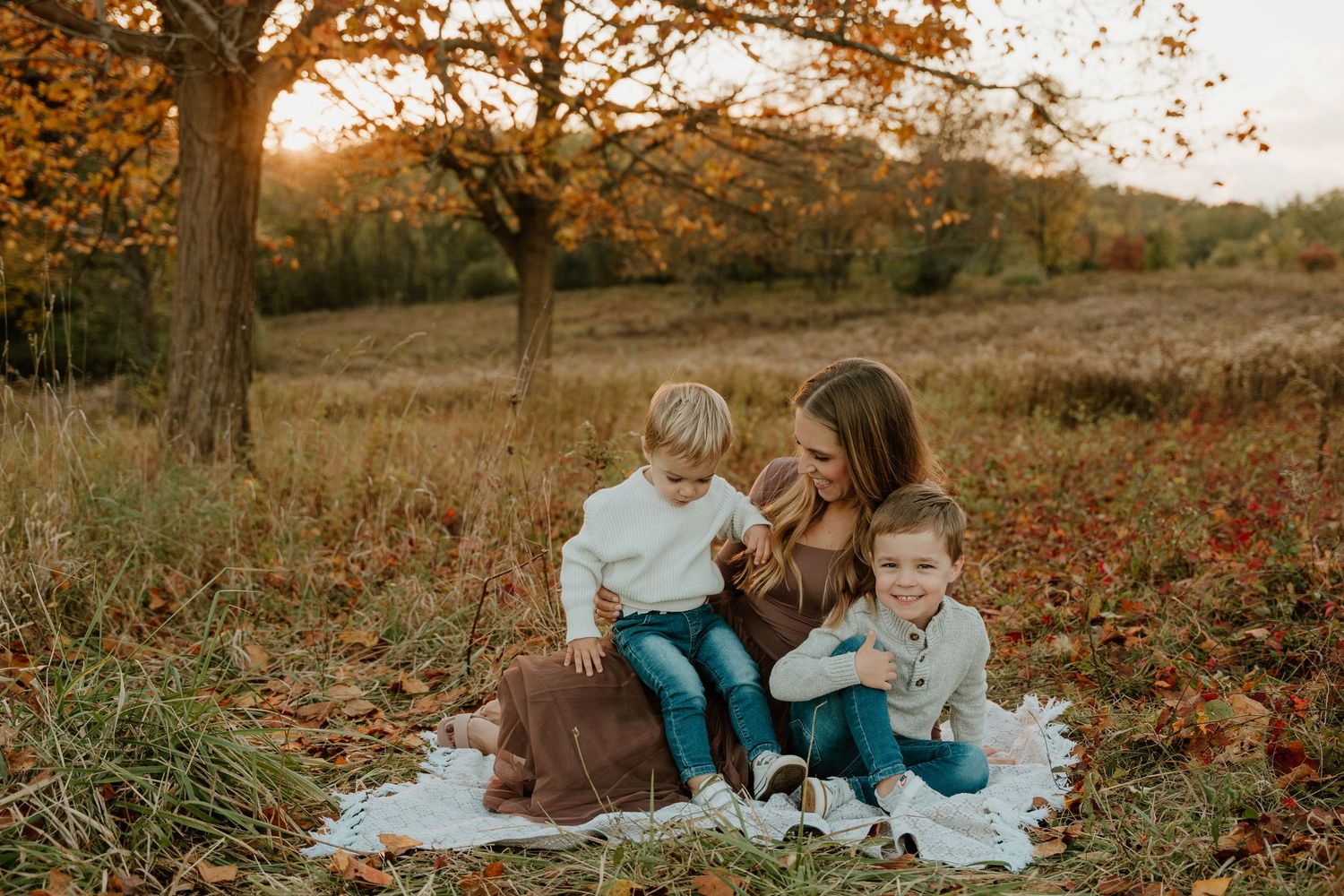 Family enjoying autumn season together in a park with fallen leaves during golden hour sunset.