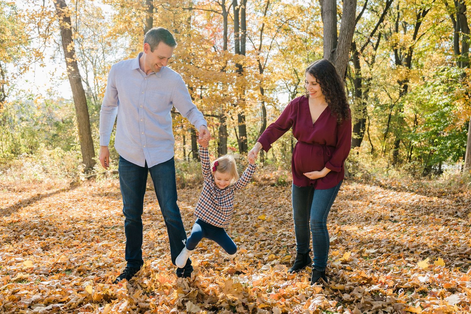 A family plays together in autumn leaves on a sunny fall day in the woods.
