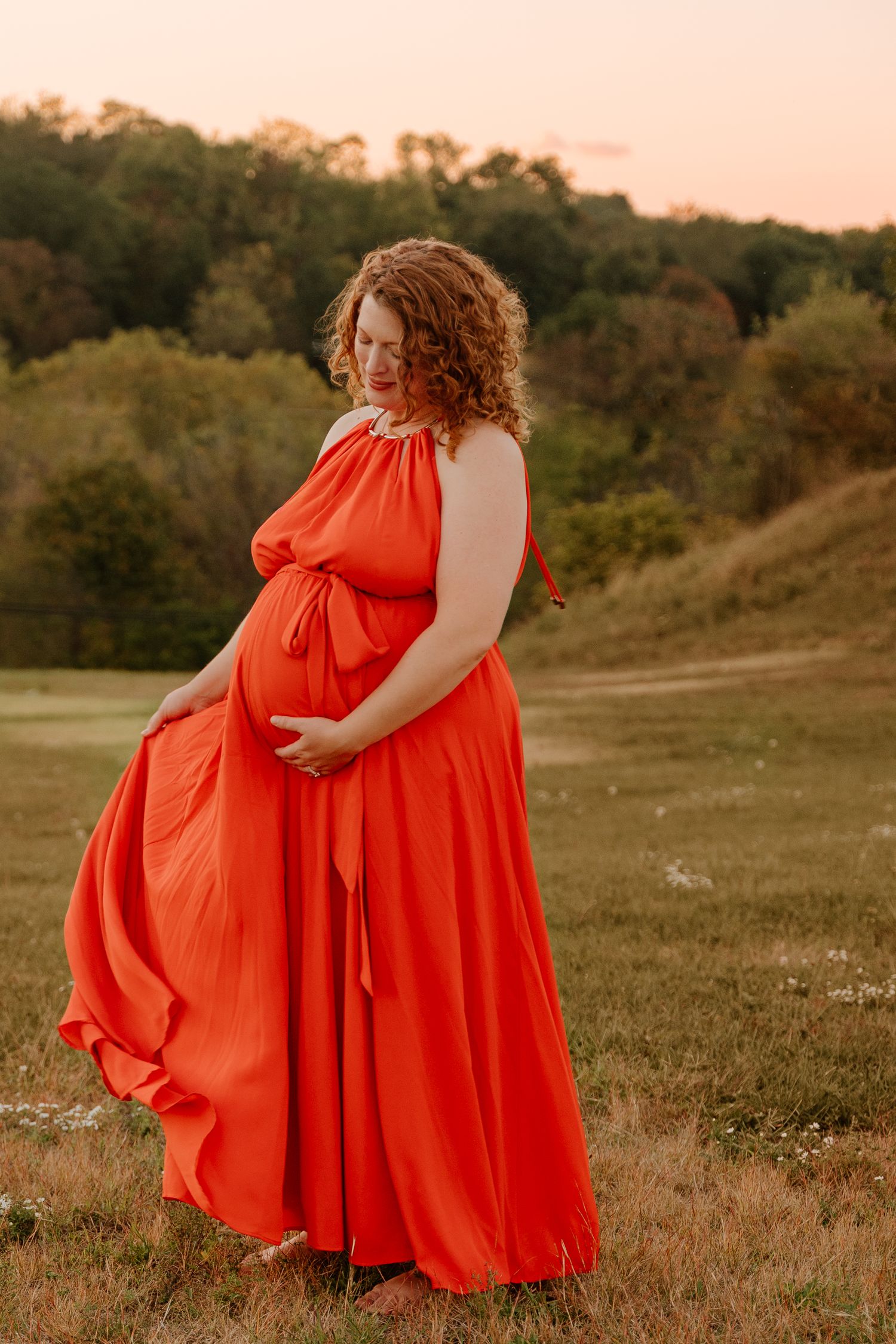 A flowing red dress twirls gracefully in a golden sunset field creating an ethereal summer scene.