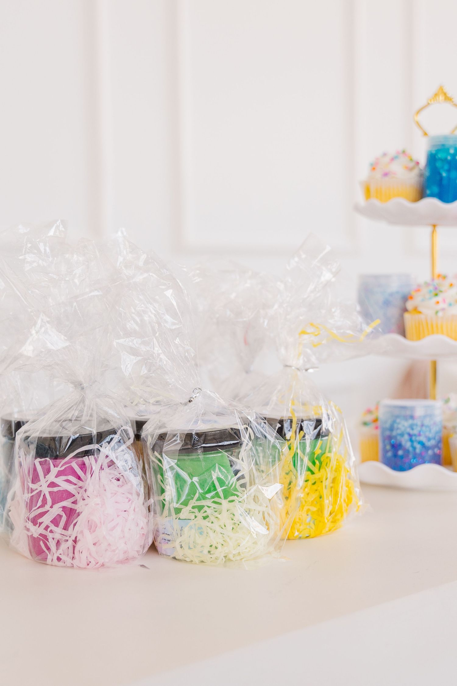Colorful shredded paper gift packaging in clear cellophane bags displayed on white surface with party decorations in background.