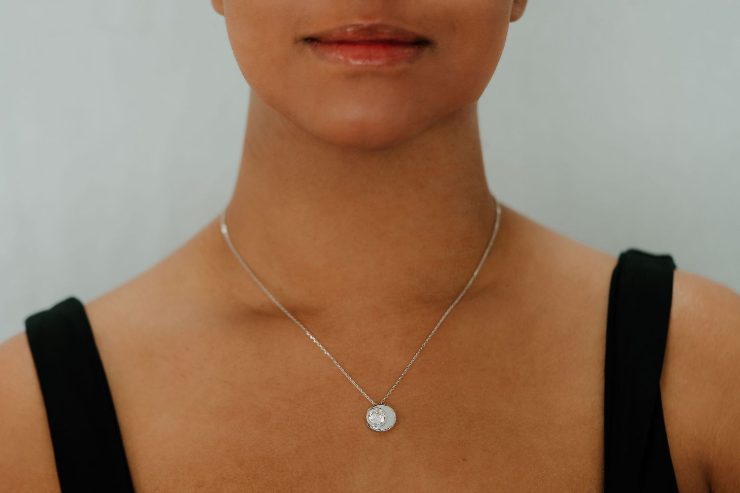 A person wearing a black tank top and silver necklace poses in front of a light colored background.