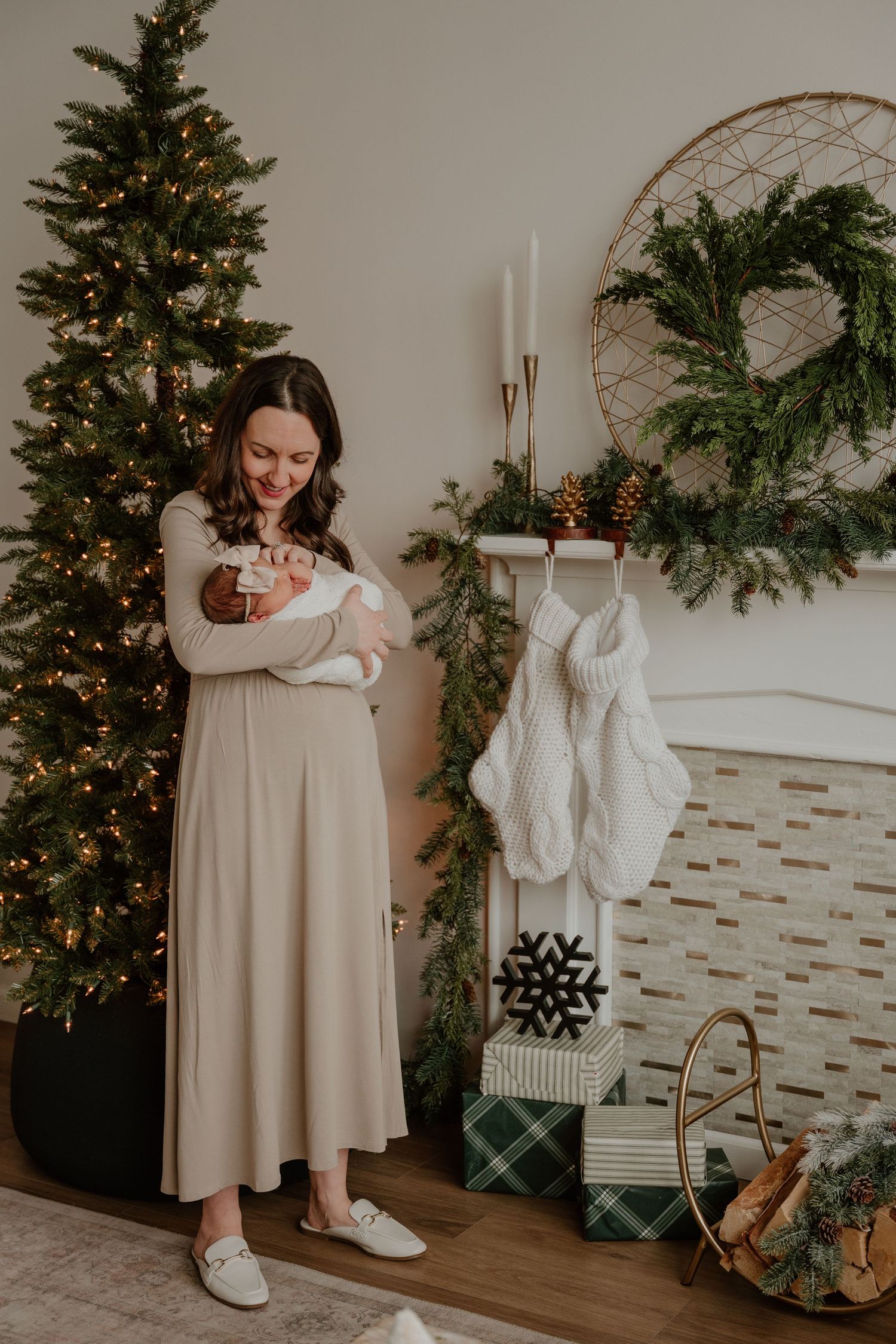 A cozy Christmas scene with decorated tree, wreath, stockings and candles in a warm neutral-toned living room setting.
