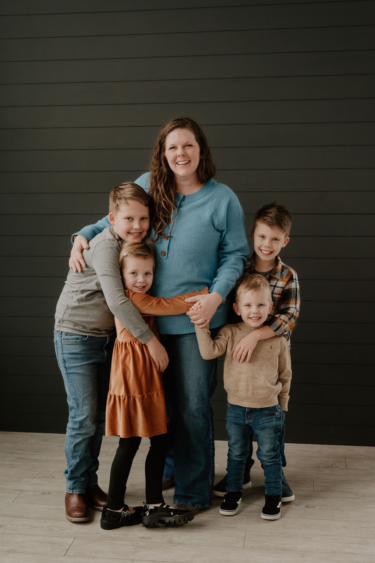 A family group poses together against a dark green wall in coordinated casual outfits.