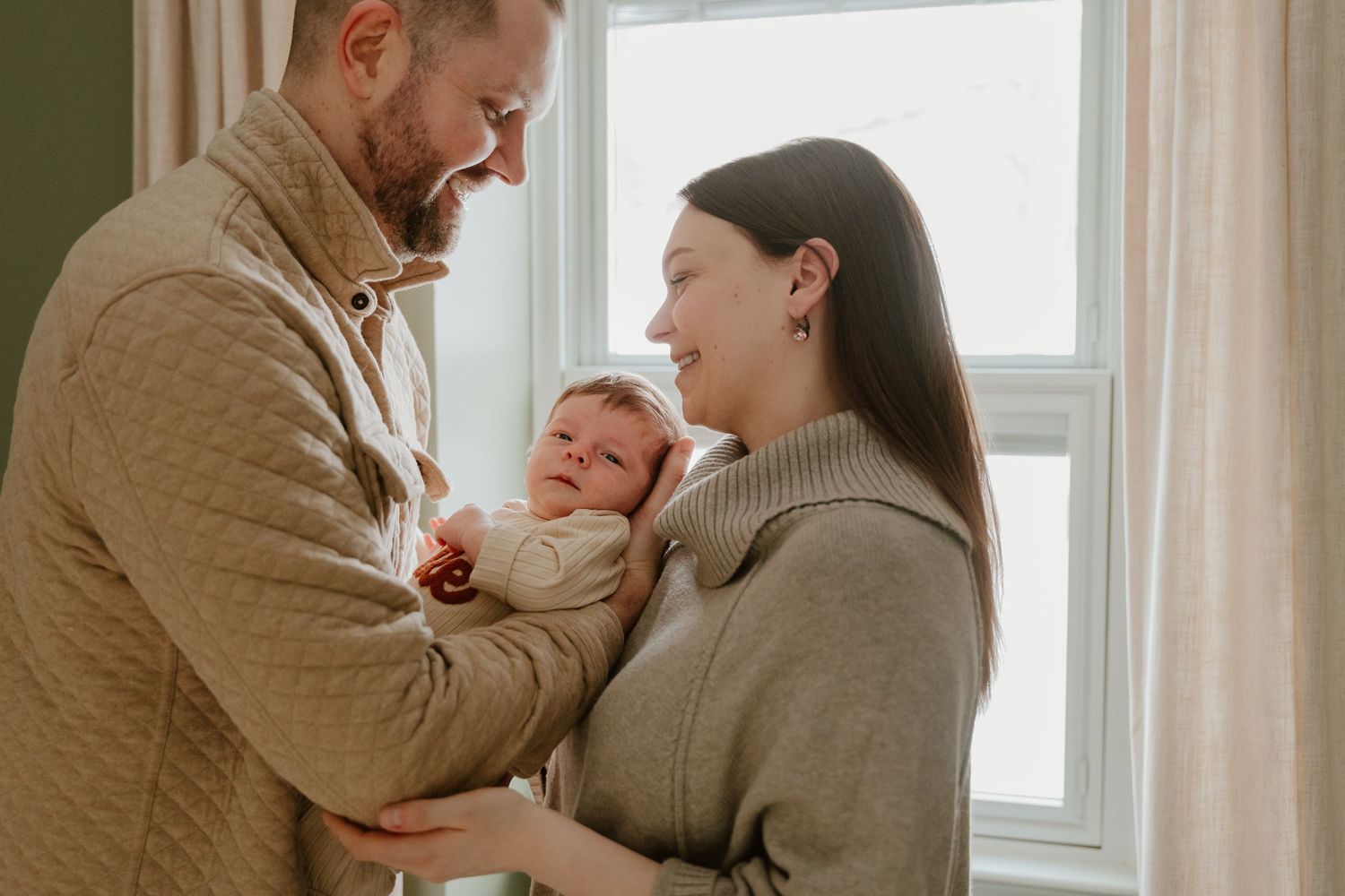 Intimate family portrait session by window with natural lighting in neutral toned clothing.