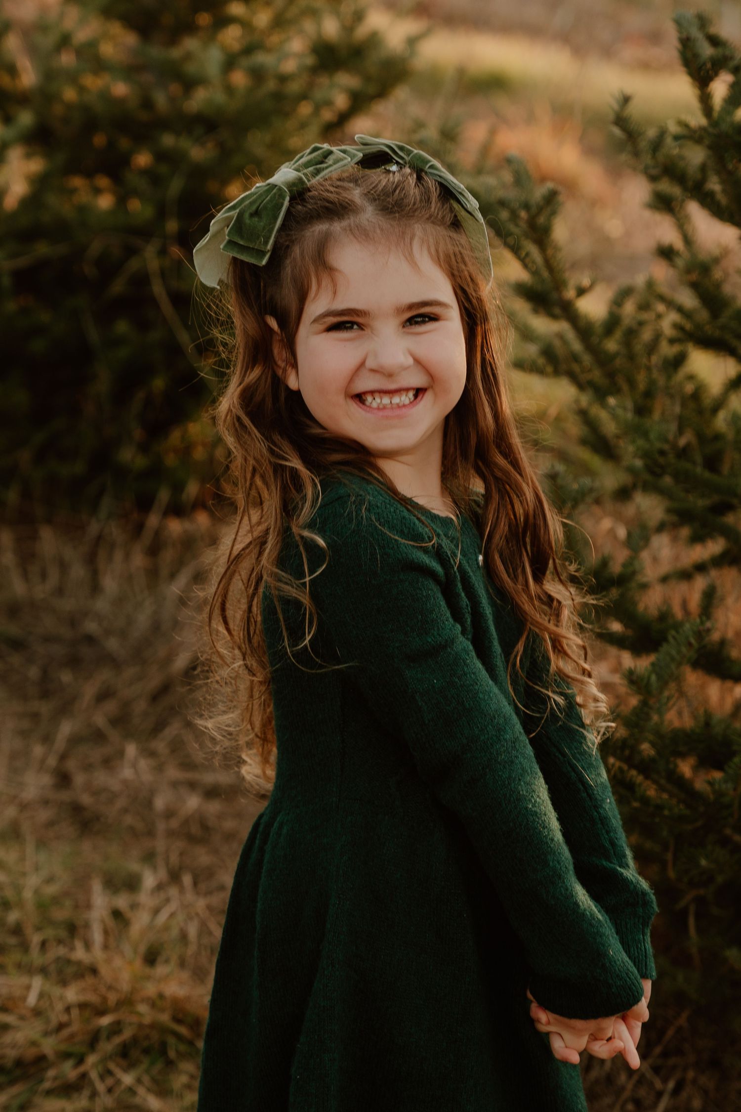 A child wearing a dark green sweater poses playfully outdoors against an autumn background.