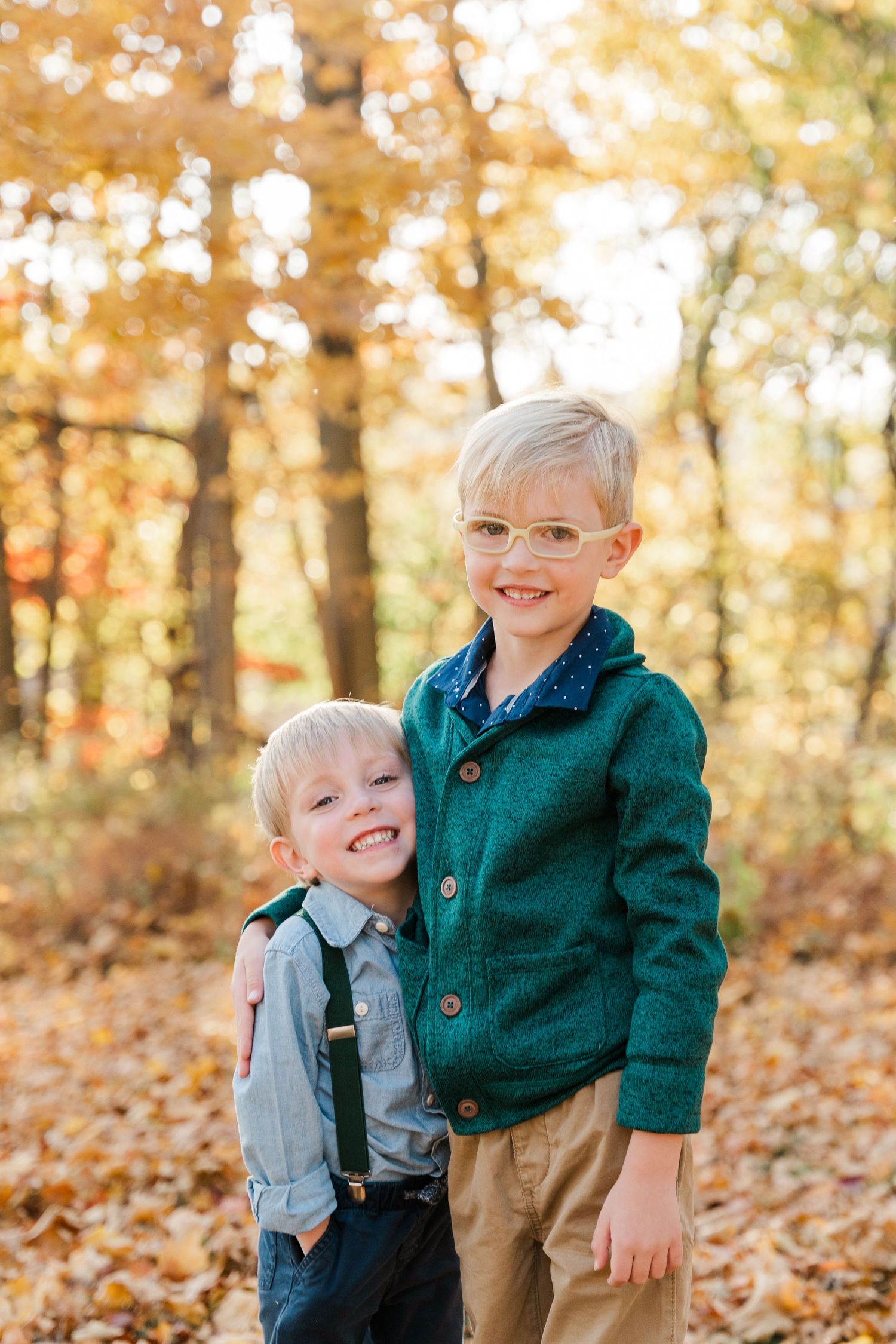 Two siblings in fall forest wearing coordinating green sweaters.