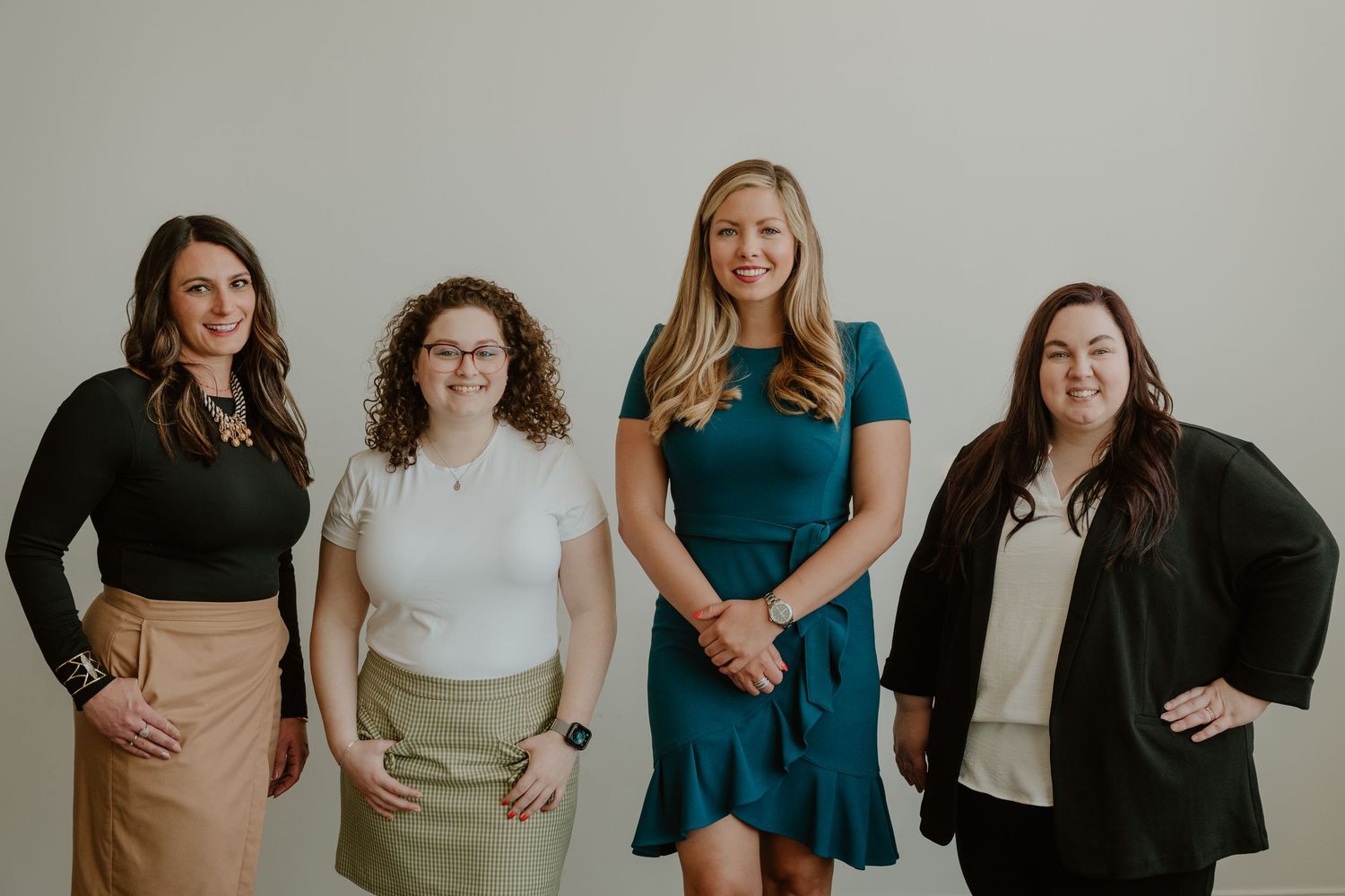 Group of people wearing casual business attire pose together against a white wall.