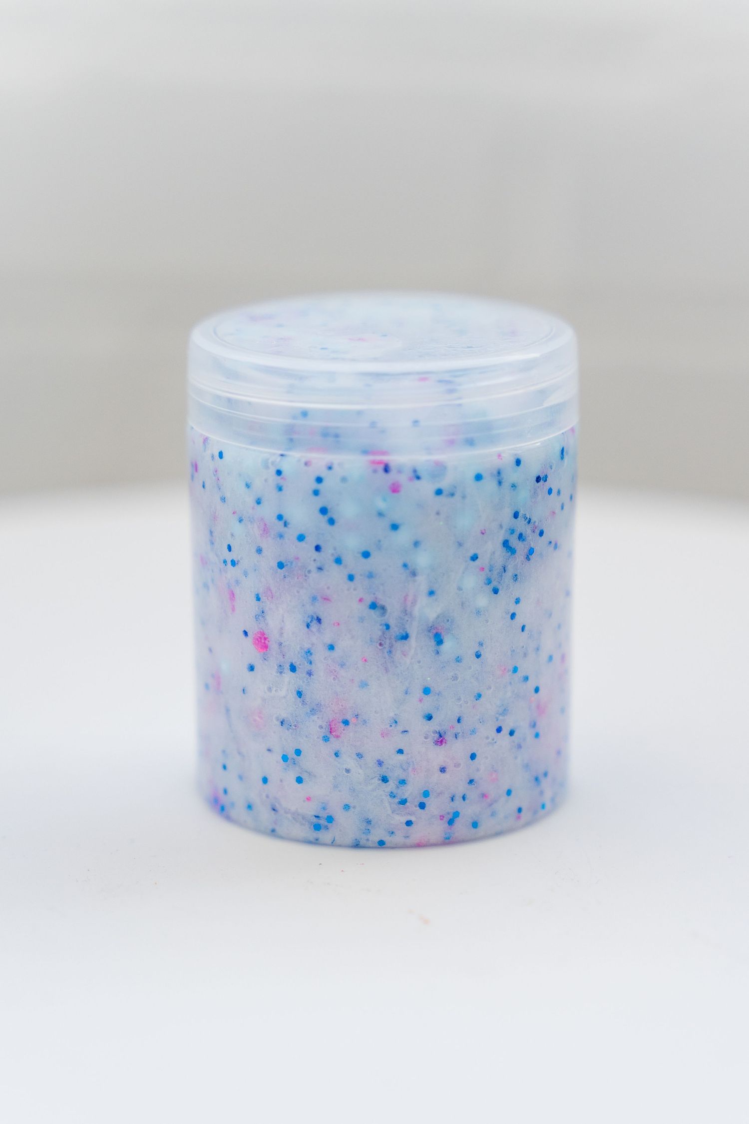 A clear plastic jar filled with sparkly blue and pink glitter slime against a light background.