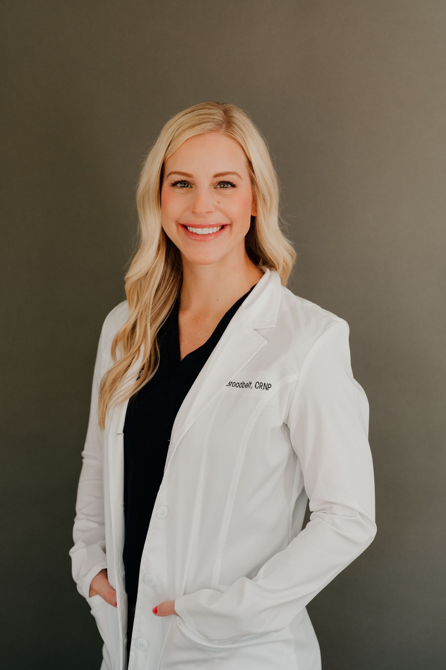 Healthcare professional in white lab coat and black top poses for professional headshots against neutral background.