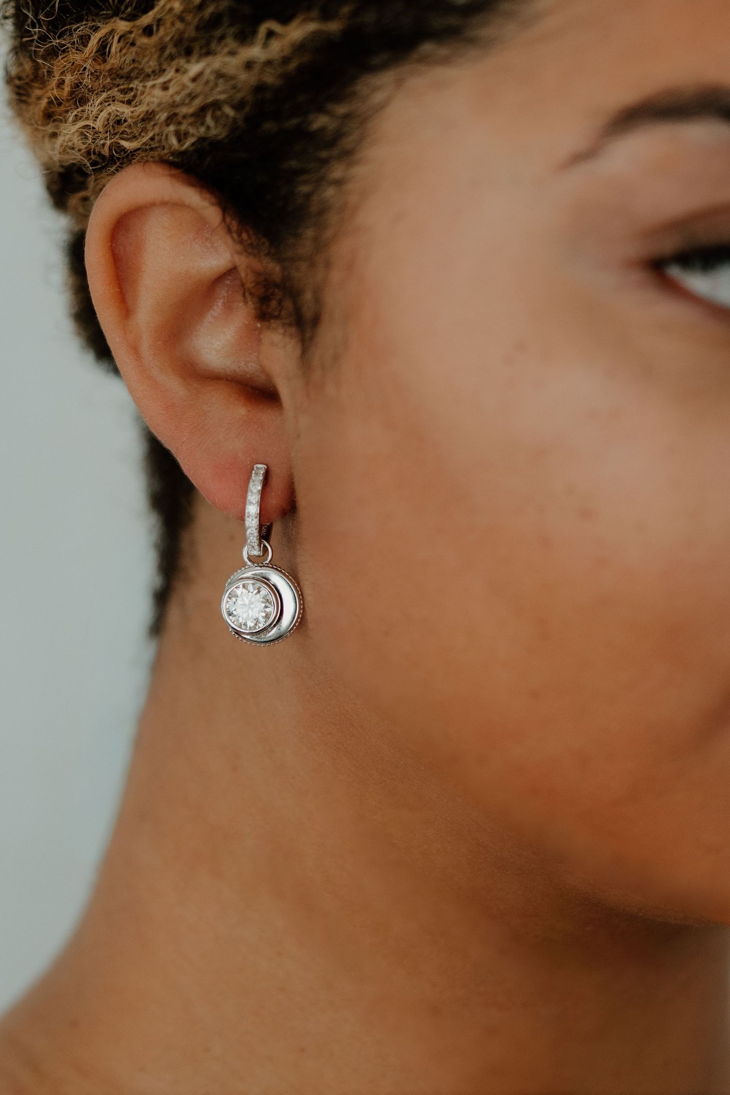 Close-up side view of a silver crescent moon earring with crystal details against a blurred background.