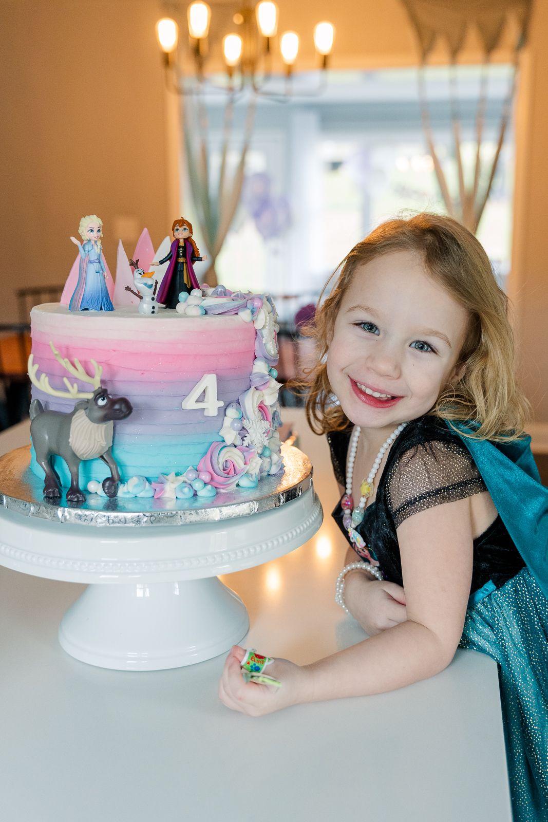 Beautiful Frozen-themed birthday cake with Elsa and Anna figurines on a white cake stand with pink and blue gradient icing.