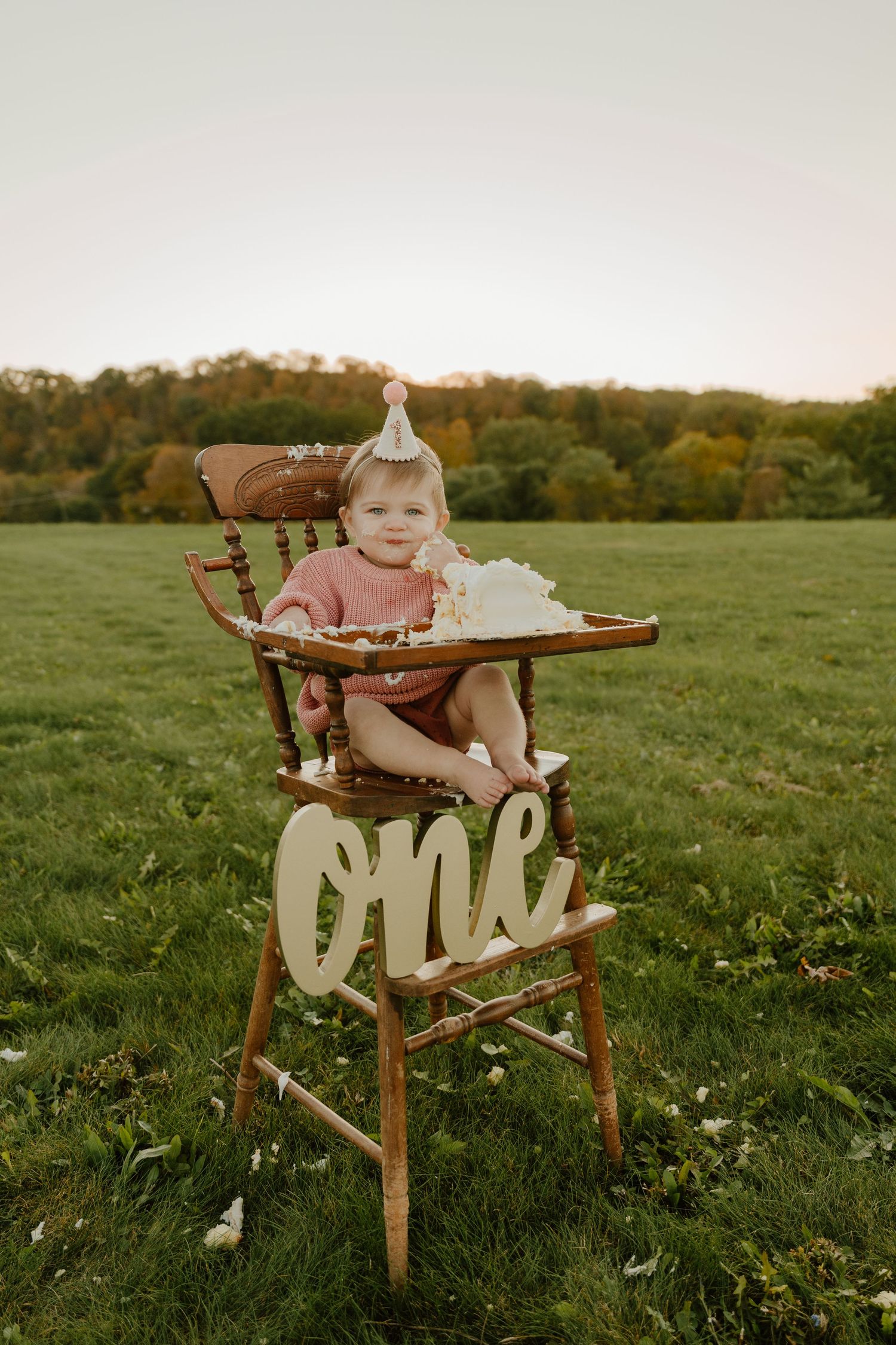 Vintage wooden high chair sits in a grassy meadow at sunset with a rustic farmhouse aesthetic.