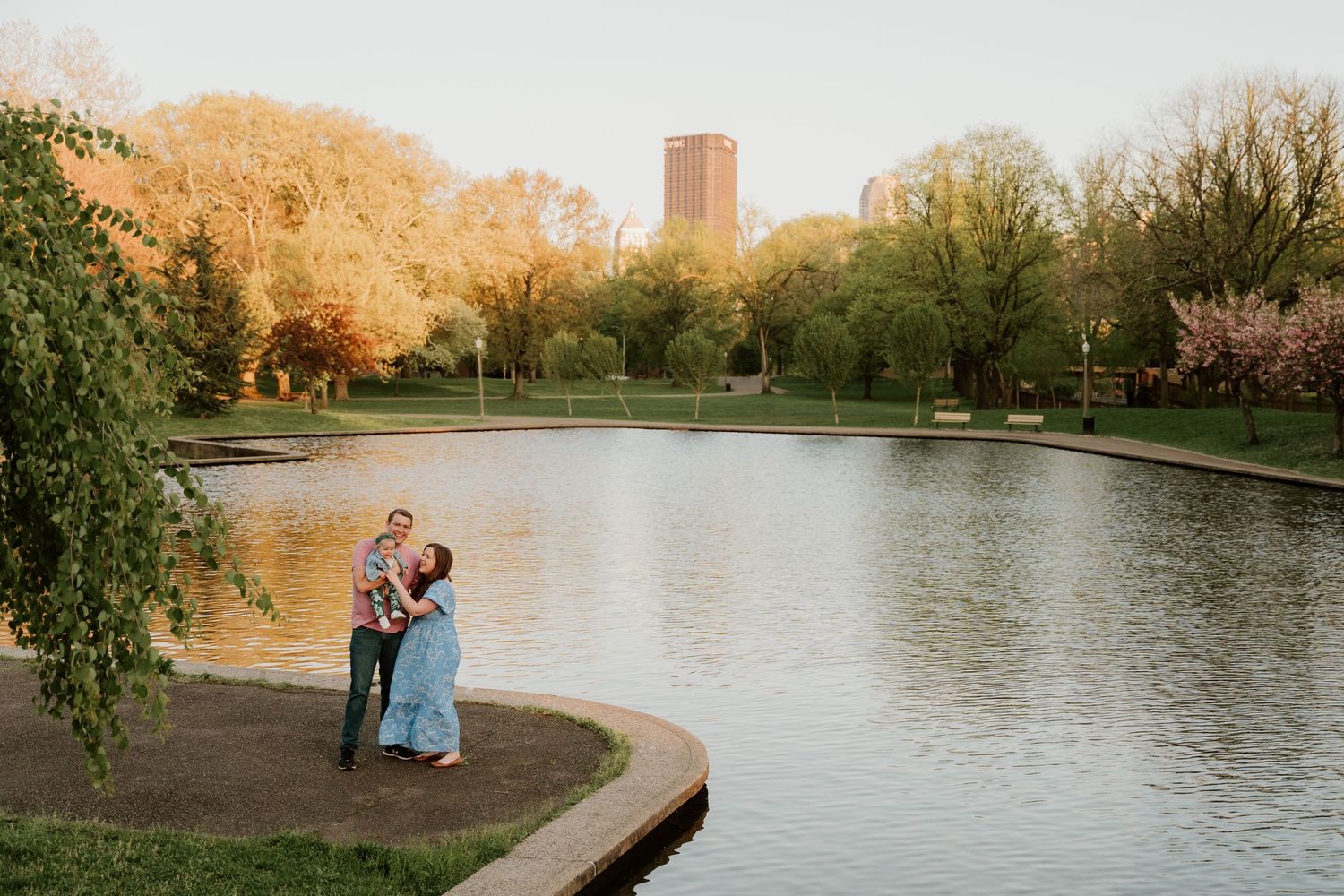 Couple sharing romantic moment by lake during golden sunset with city building in background.
